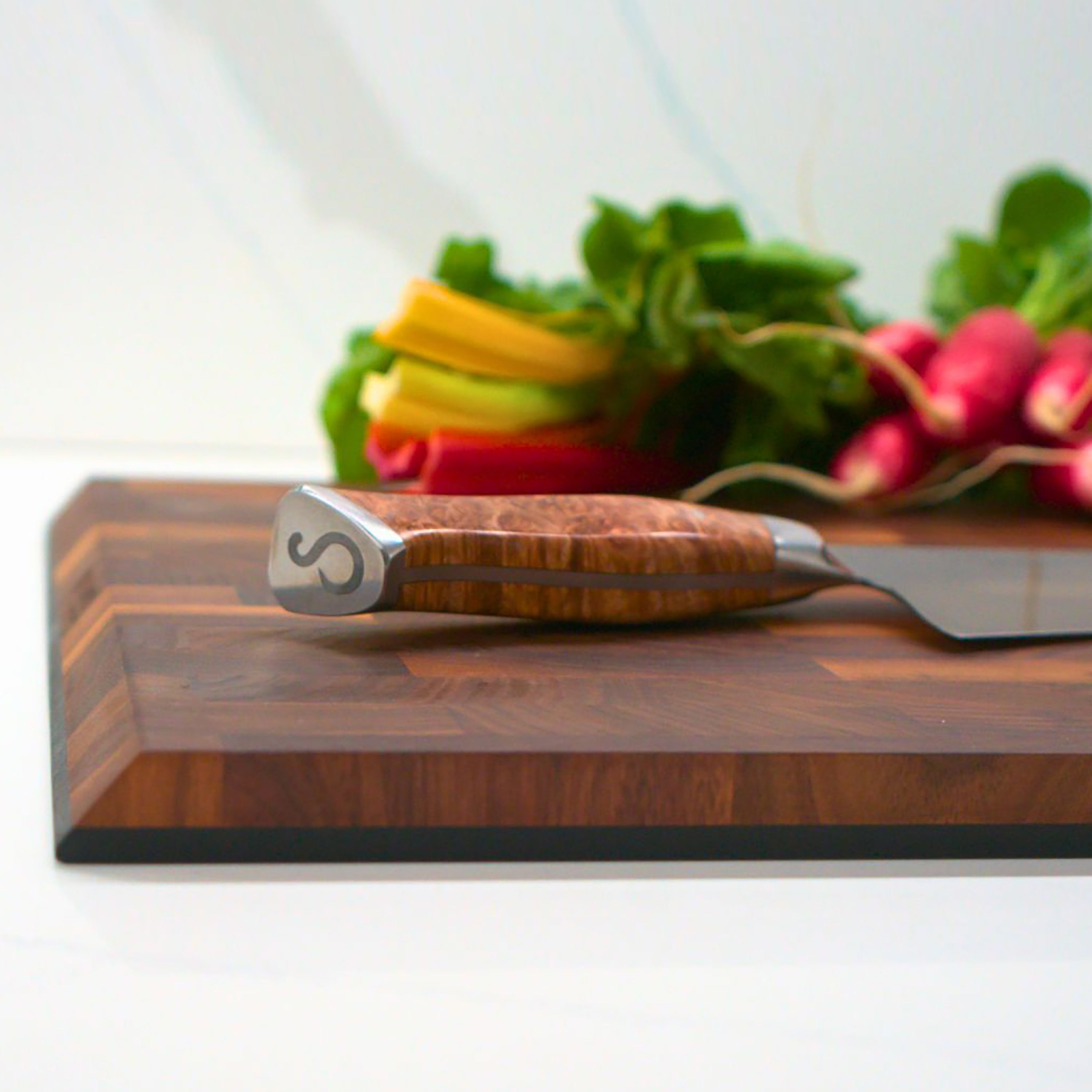 Hand holding the beveled handle of the walnut cutting board for easy grip and maneuverability