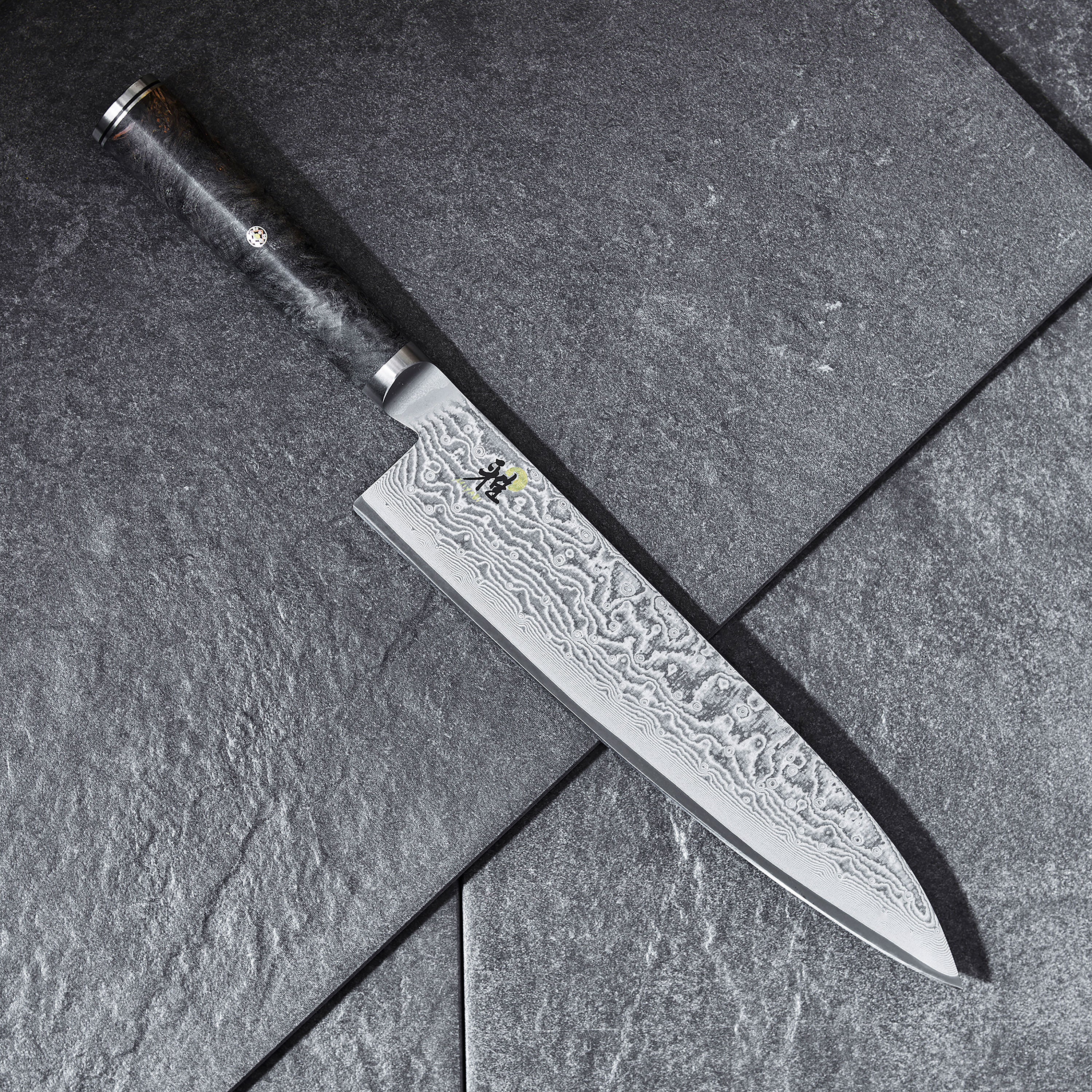 Miyabi Black chefs knife in action, slicing through fresh vegetables on a kitchen counter.