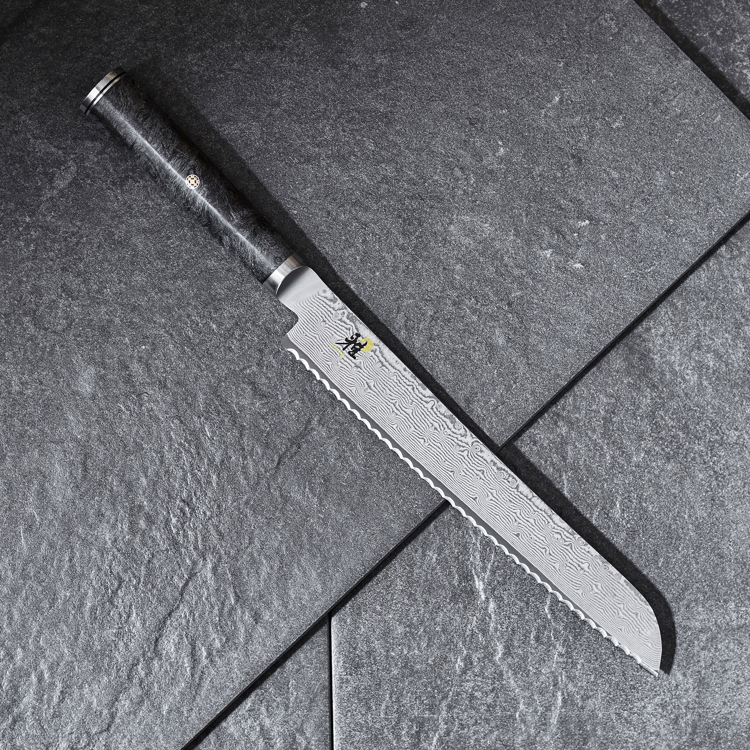 Miyabi Black 9-Inch Damascus Bread Knife from the side, highlighting the blades intricate Damascus pattern.