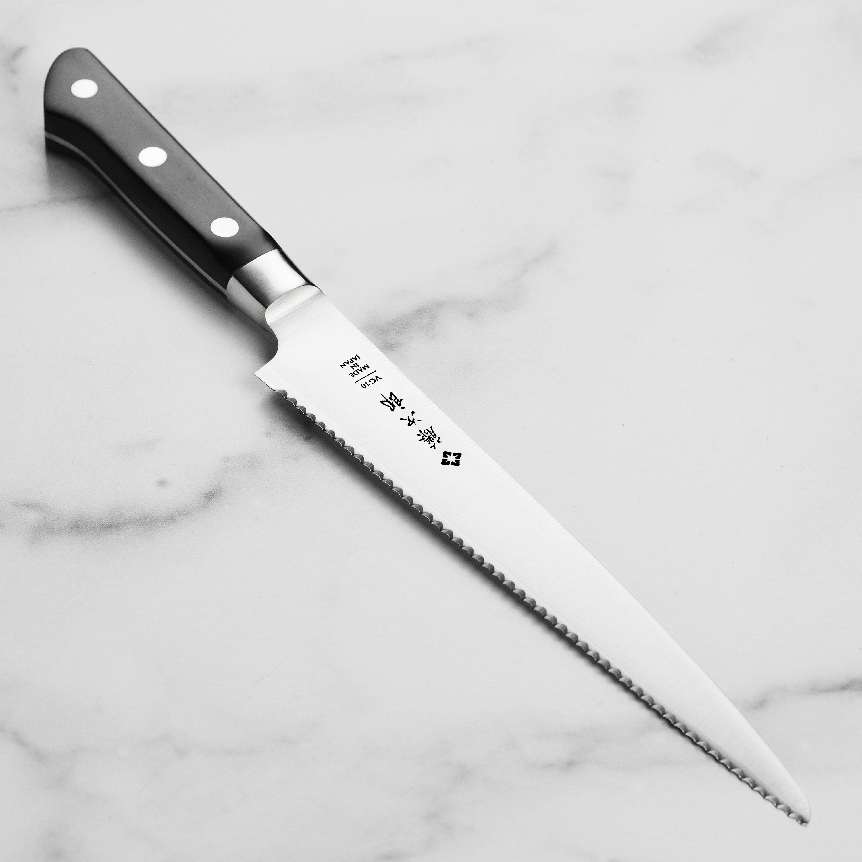 Close-up of Tojiro serrated knife slicing a rustic loaf, showcasing the VG10 steel blade