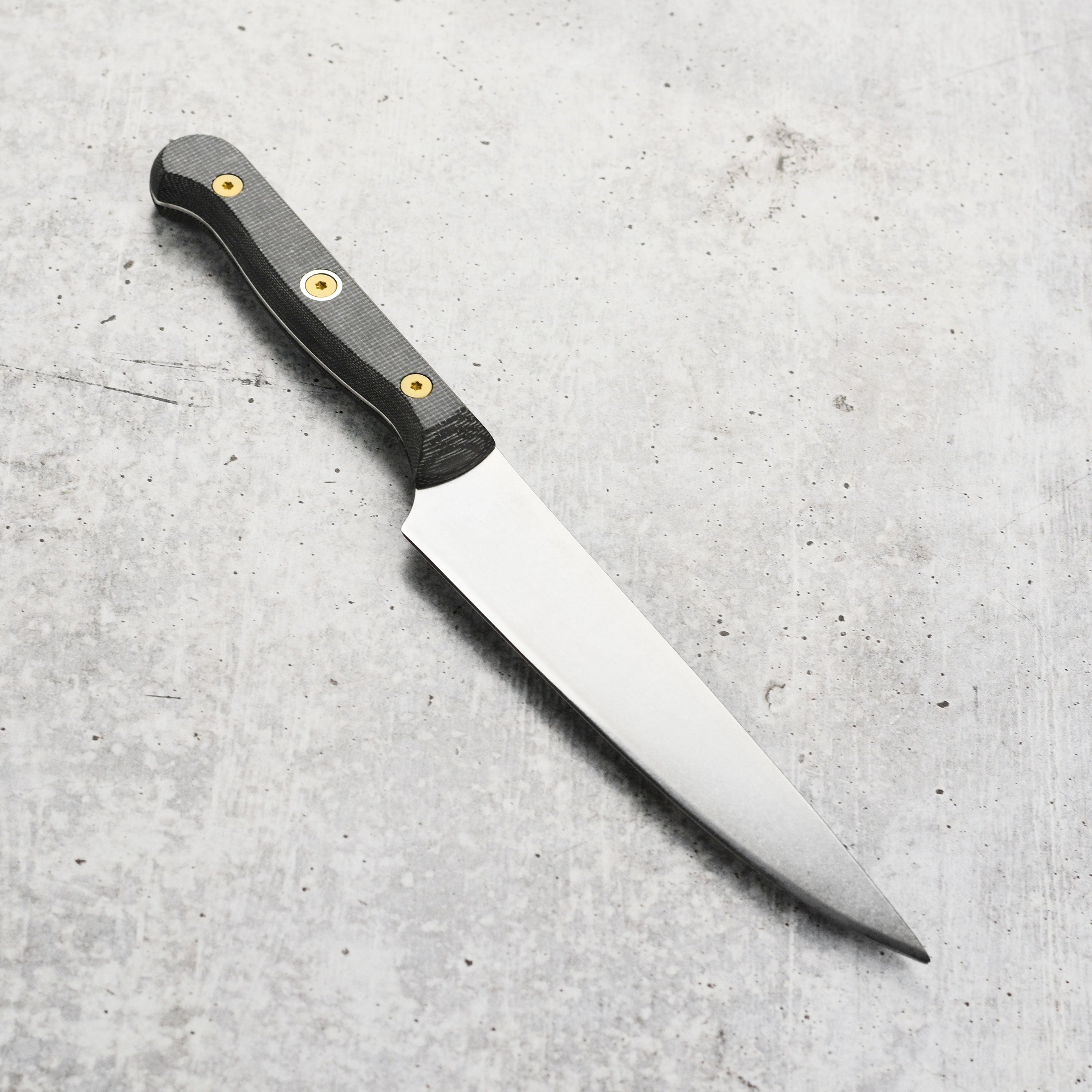 Messermeister Custom Micarta Utility Knife on a cutting board, emphasizing its sleek design and durability.