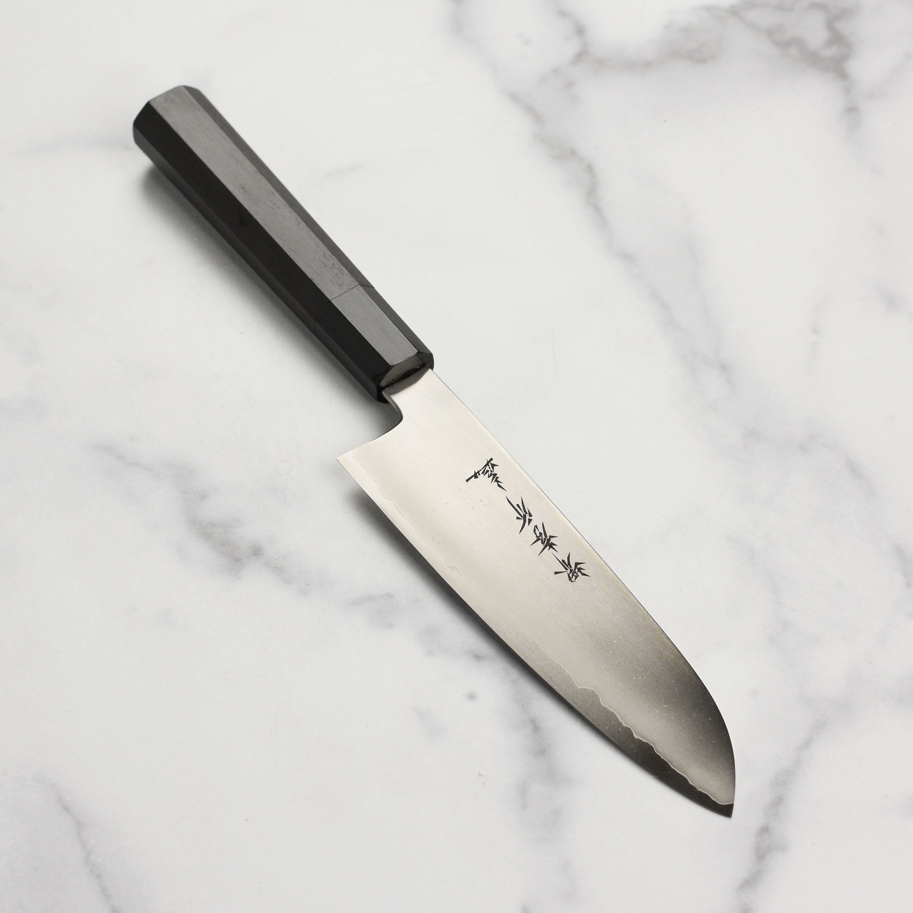 Close-up of the Sakai Ginsan hand-forged 7-inch Santoku knife highlighting the blade's edge and craftsmanship.
