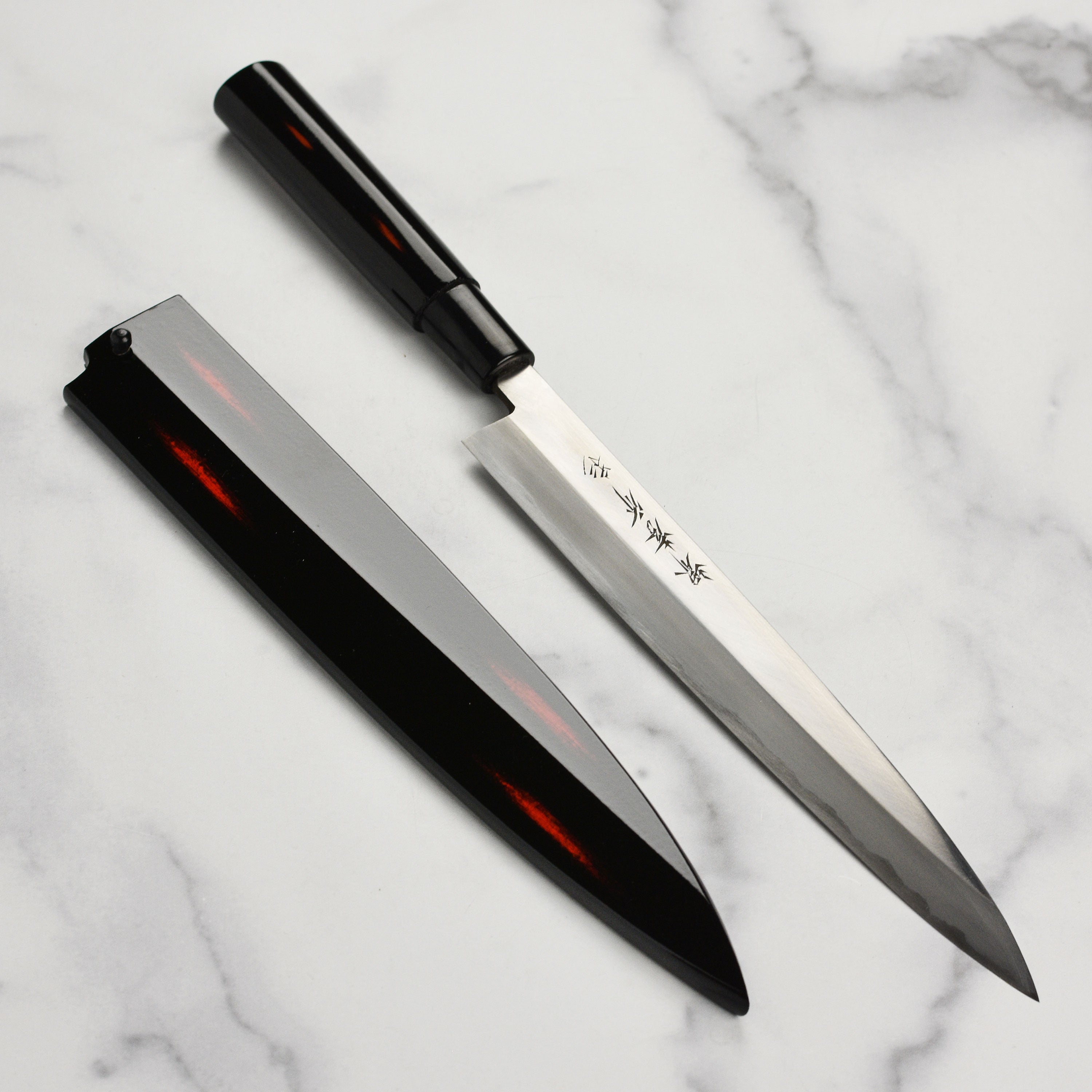 Shikisai Yanagiba knife with saya, showcasing the carbon steel blade and magnolia handle.