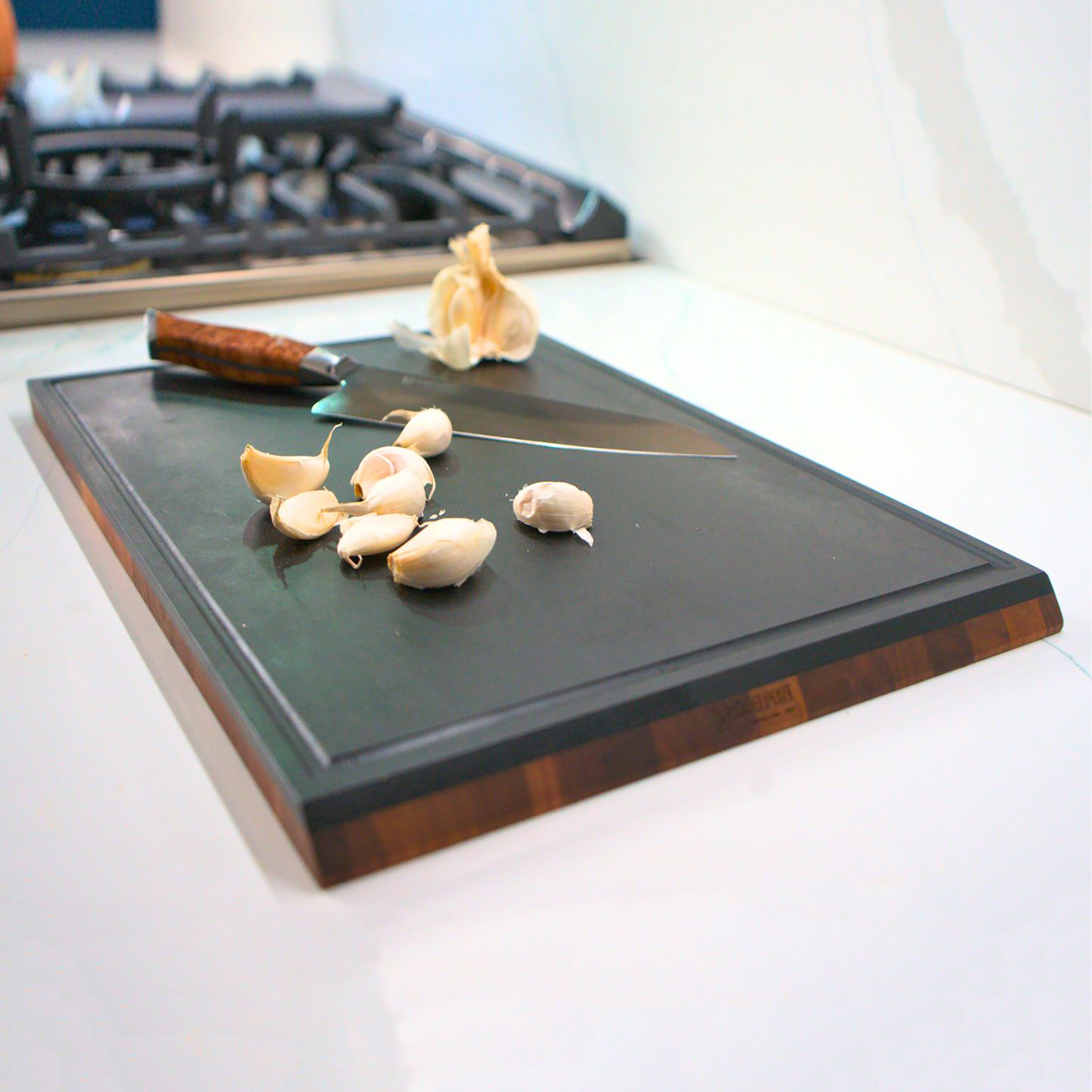 Hand holding the beveled handle of the walnut cutting board for easy grip and maneuverability