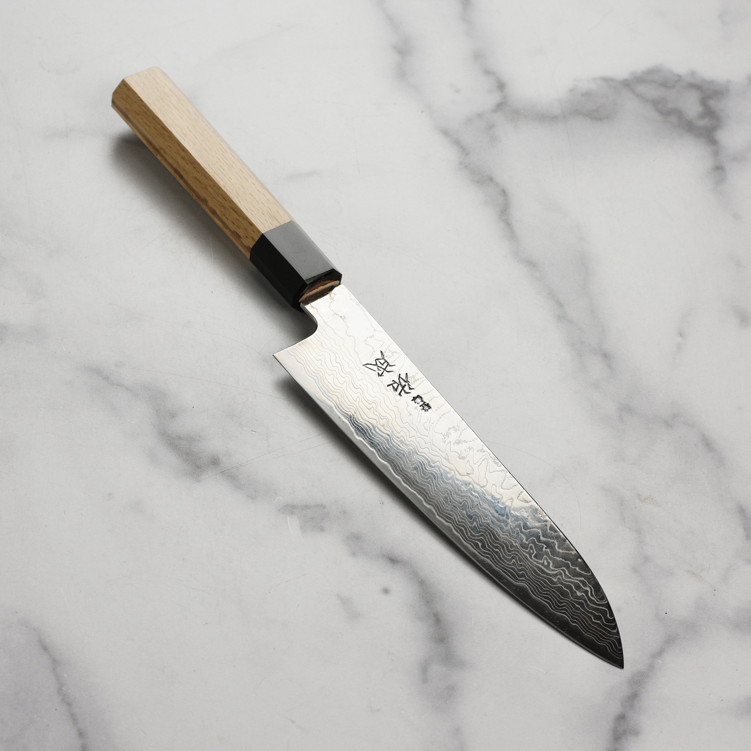 Sukenari SG2 Damascus Santoku knife held by a chef, highlighting its ergonomic handle.