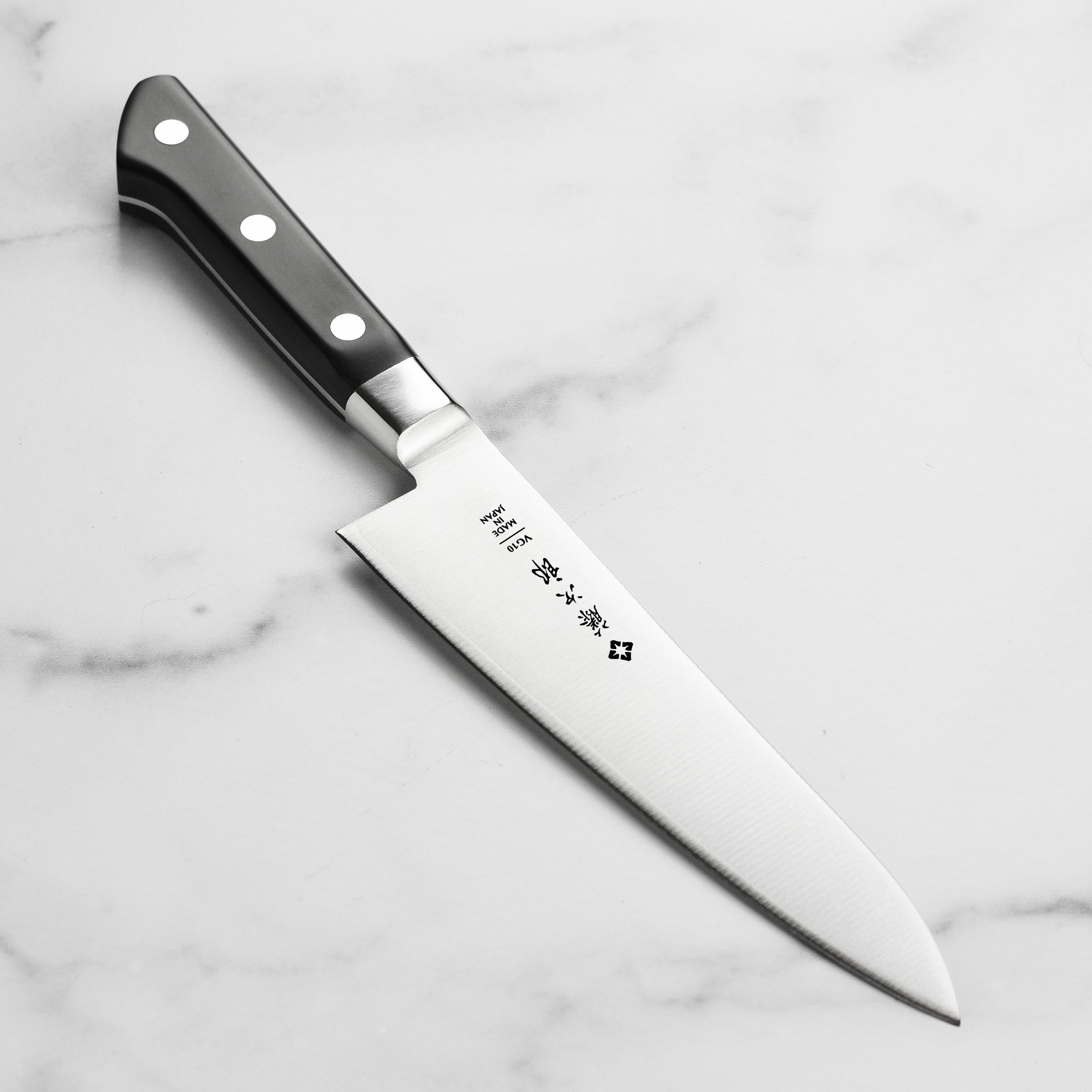 Close-up of Tojiro Classic 7-inch chef's knife on a wooden cutting board, showcasing the VG-10 steel blade and micarta handle.