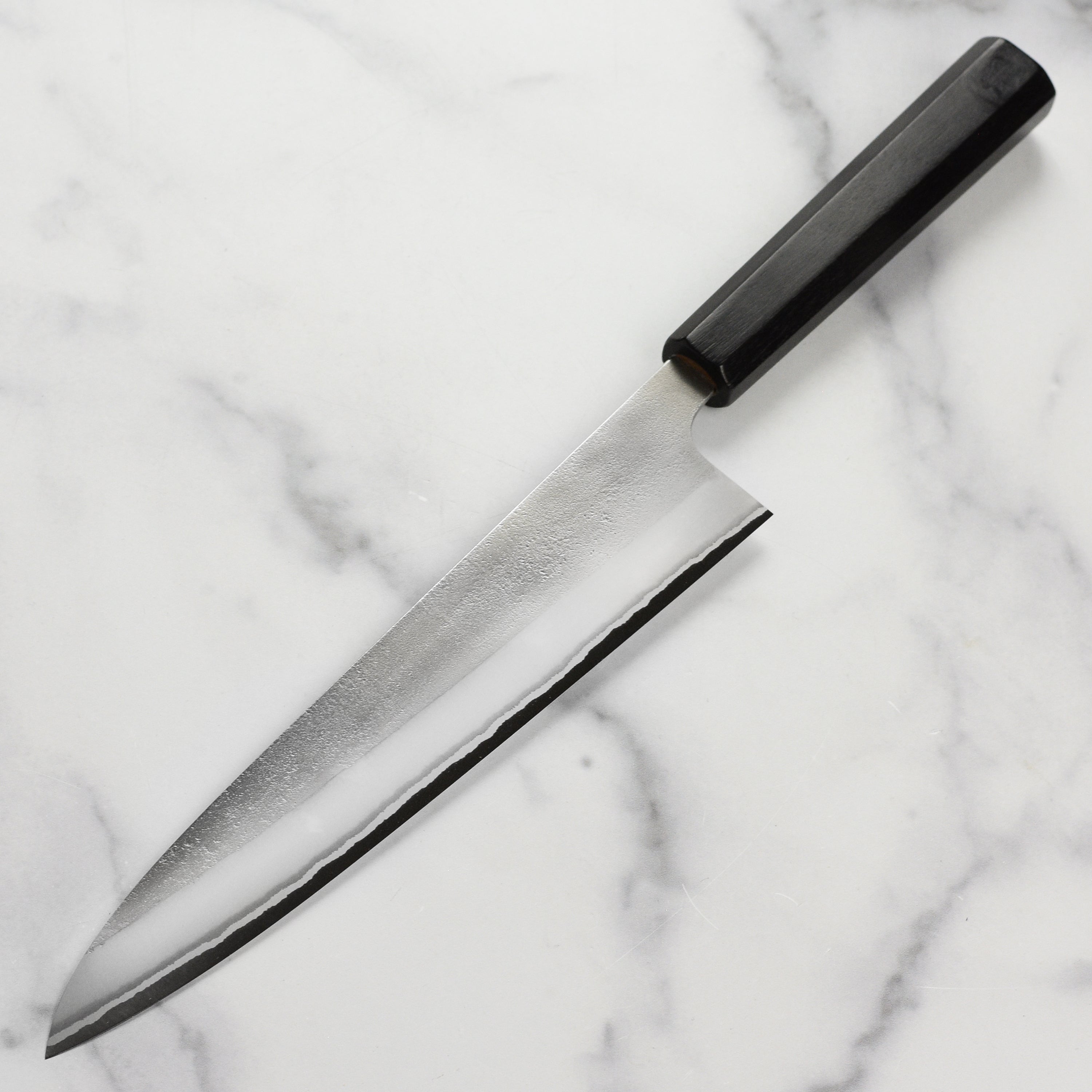 Japanese gyuto knife slicing vegetables on a cutting board, focus on blade