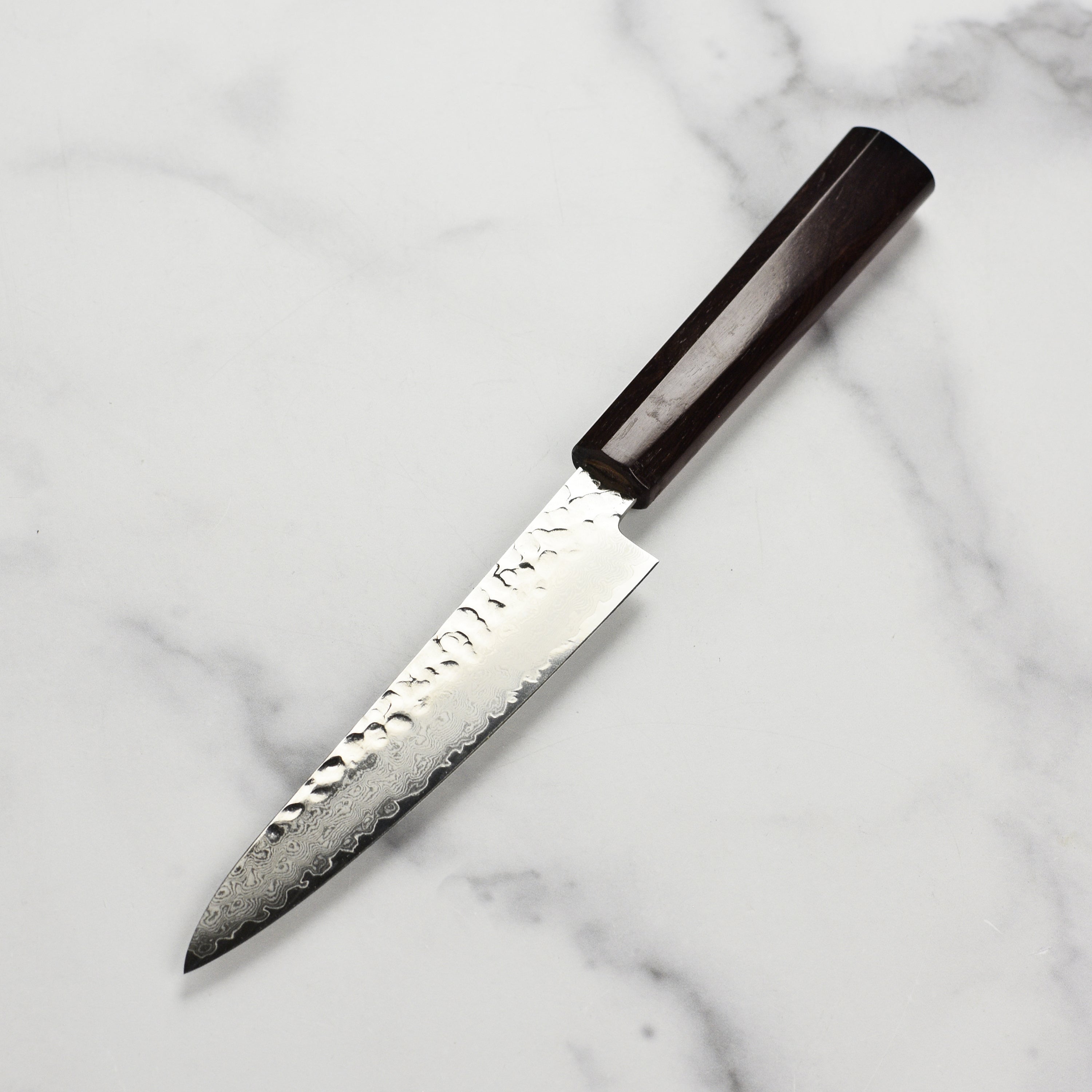 Takayuki Tsuchime Damascus petty knife in action, slicing fresh vegetables on a wooden cutting board.
