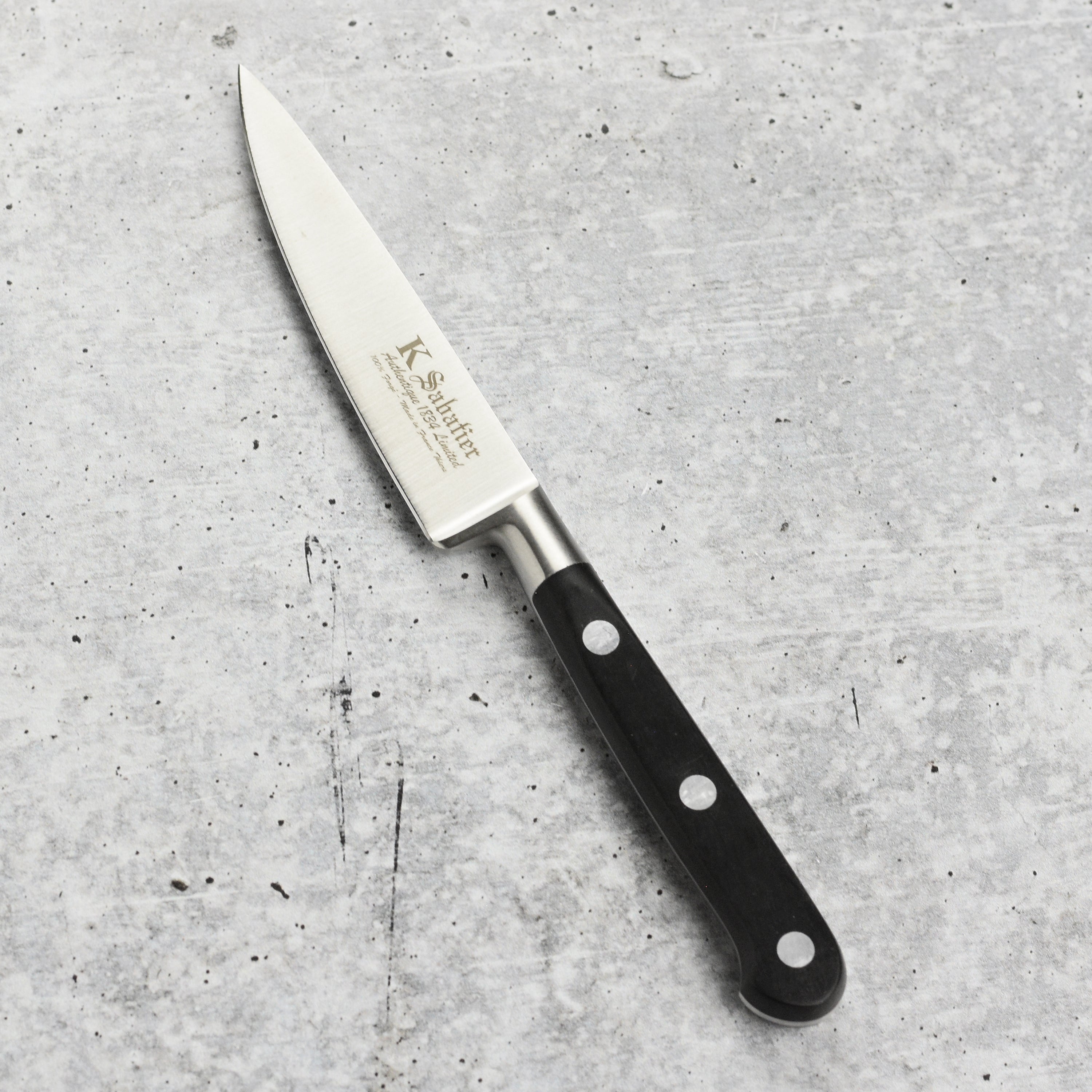 K Sabatier paring knife being used to slice fresh fruits and vegetables on a cutting board.