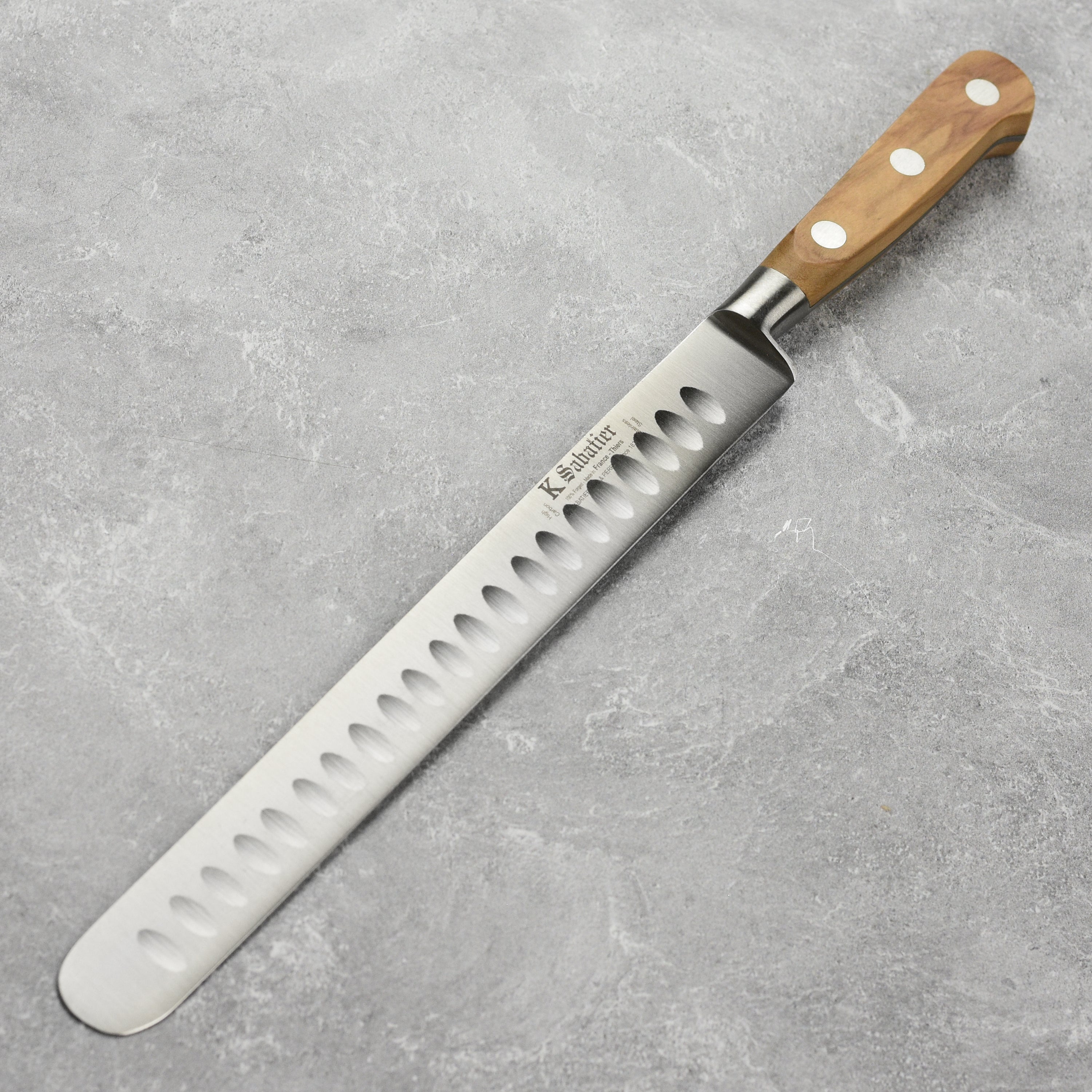 K Sabatier olive wood slicing knife from the side, highlighting the elegant handle and blade.