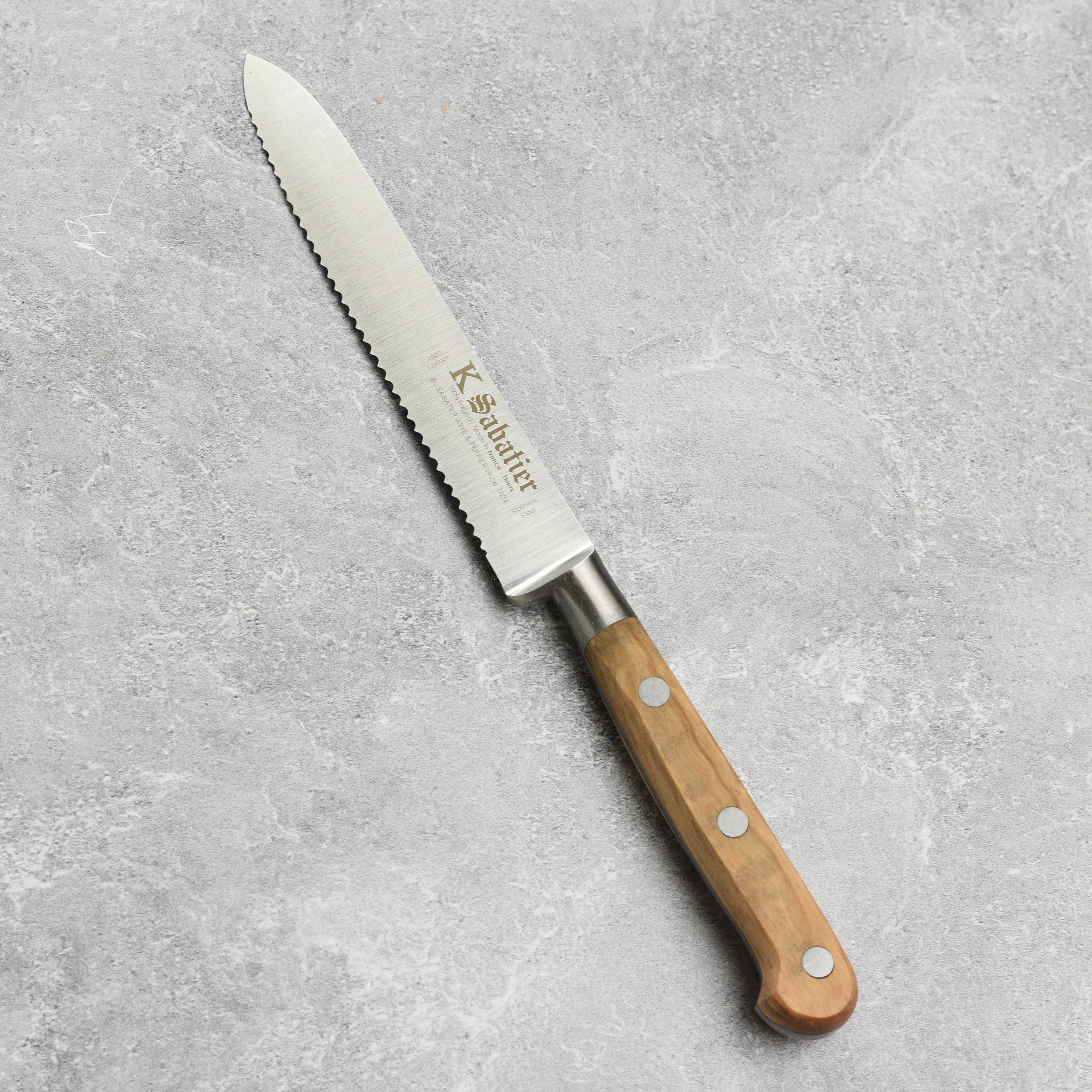 Close-up of K Sabatier olive wood knife showing serrated blade and ergonomic handle