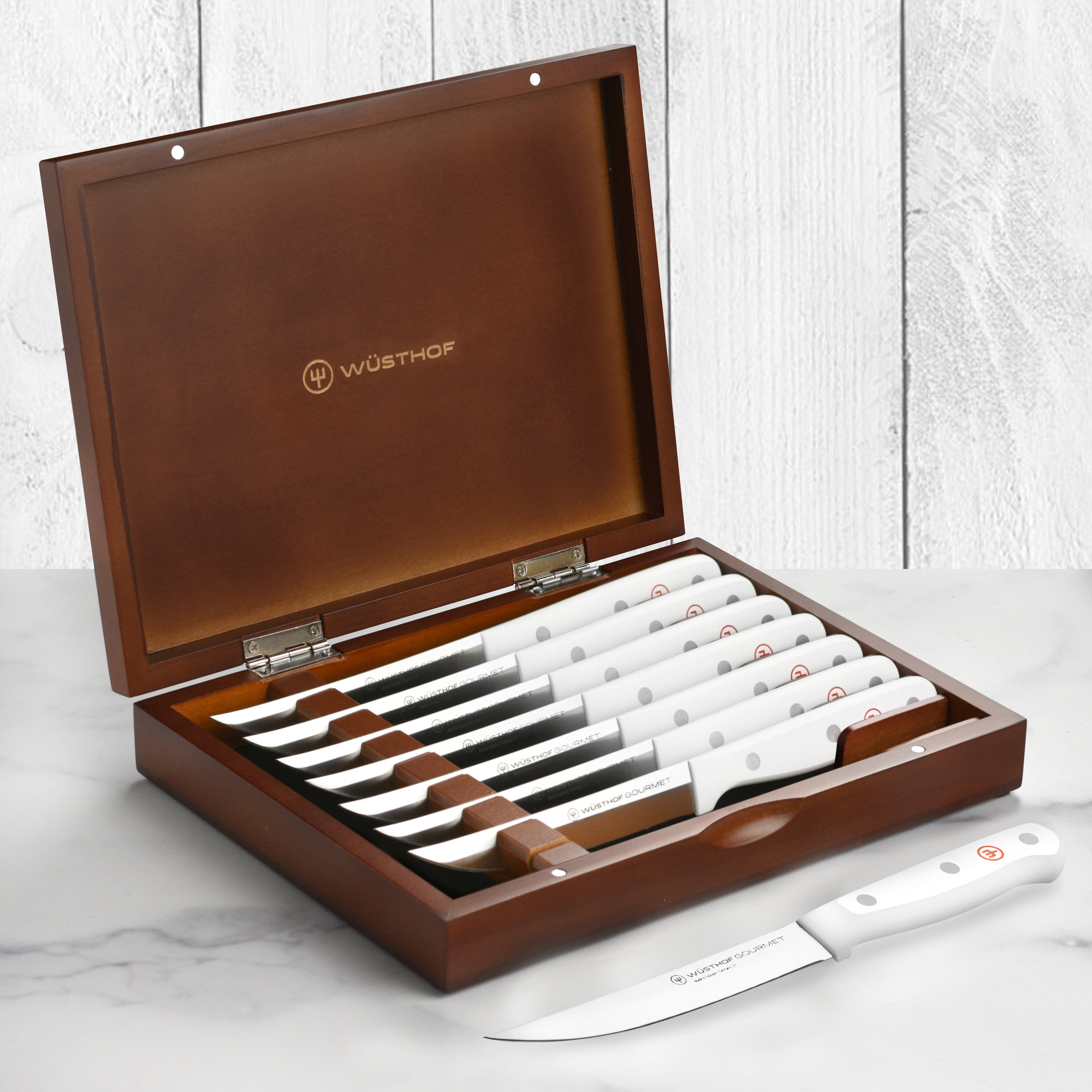 Close-up of Wusthof gourmet steak knives with white handles on a wooden cutting board