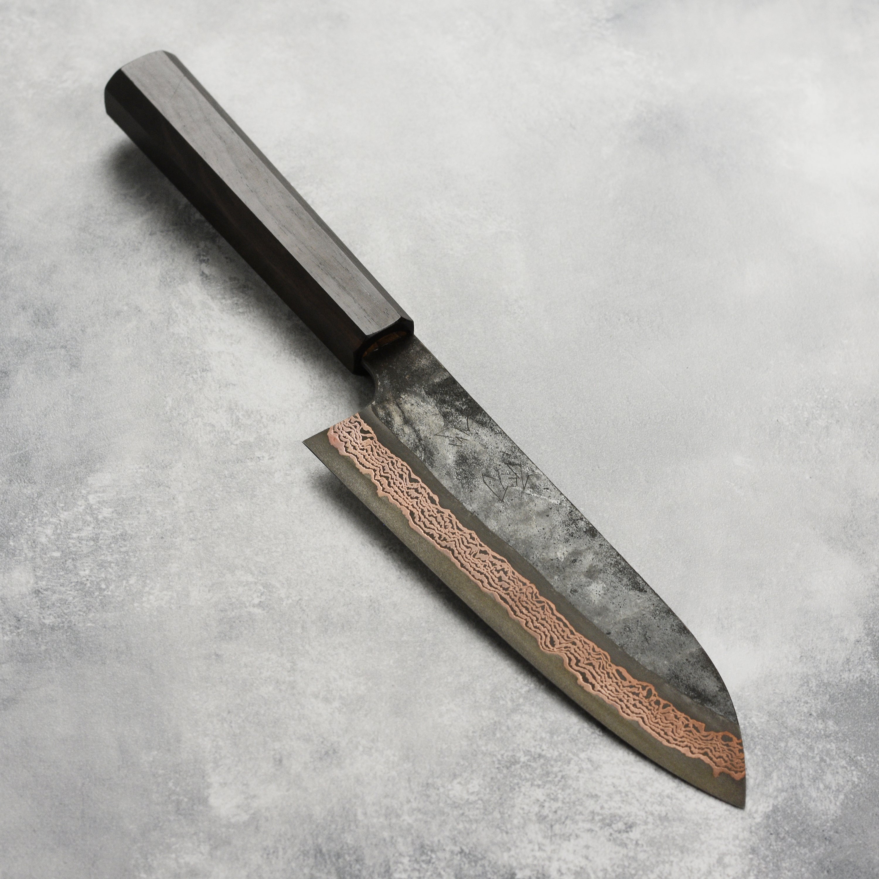 Hatsukokoro Copper Damascus Santoku Knife from the side, showcasing its sharp blade and elegant design.