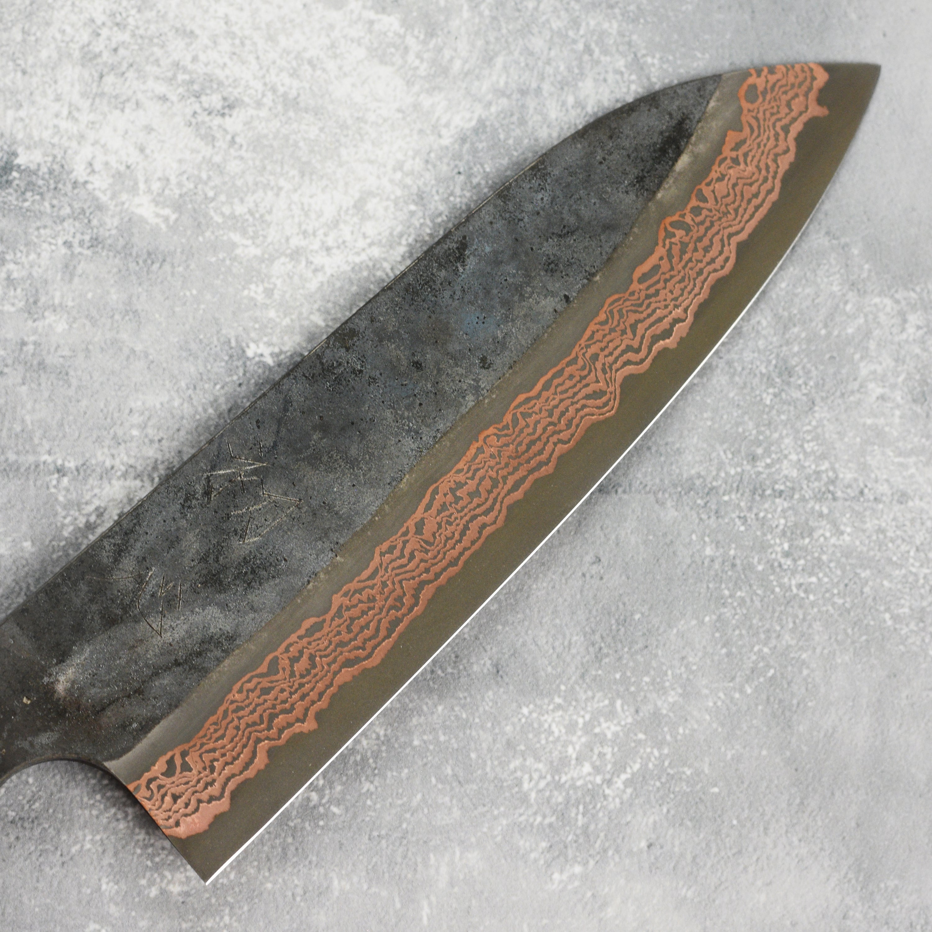 Hatsukokoro Copper Damascus Santoku Knife from the side, showcasing its sharp blade and elegant design.