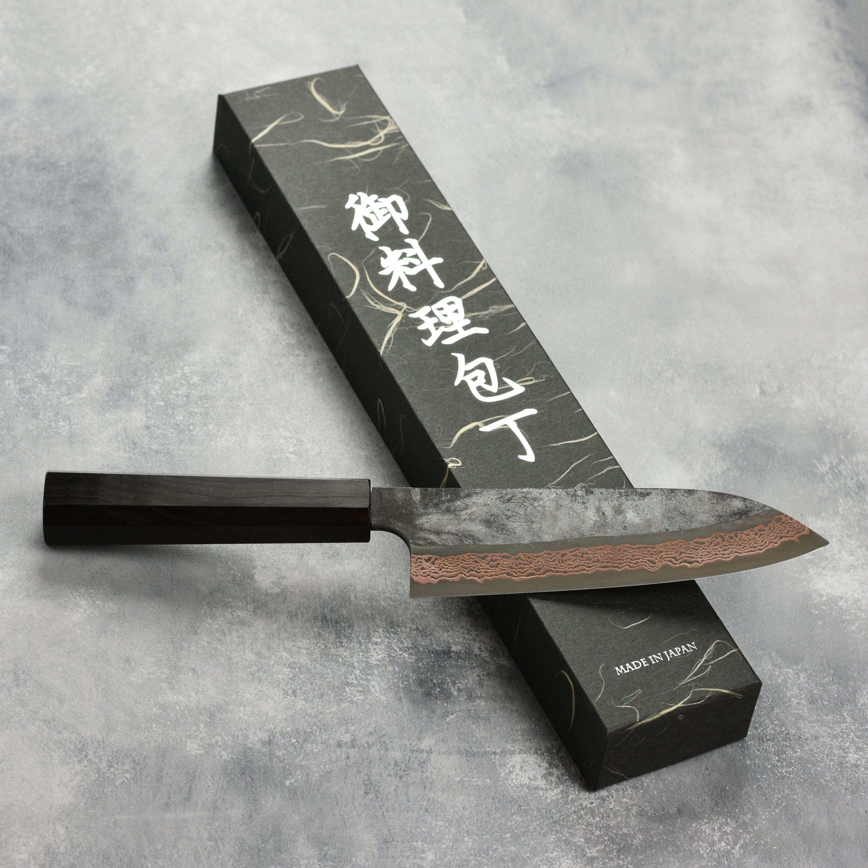 Hatsukokoro Copper Damascus Santoku Knife from the side, showcasing its sharp blade and elegant design.