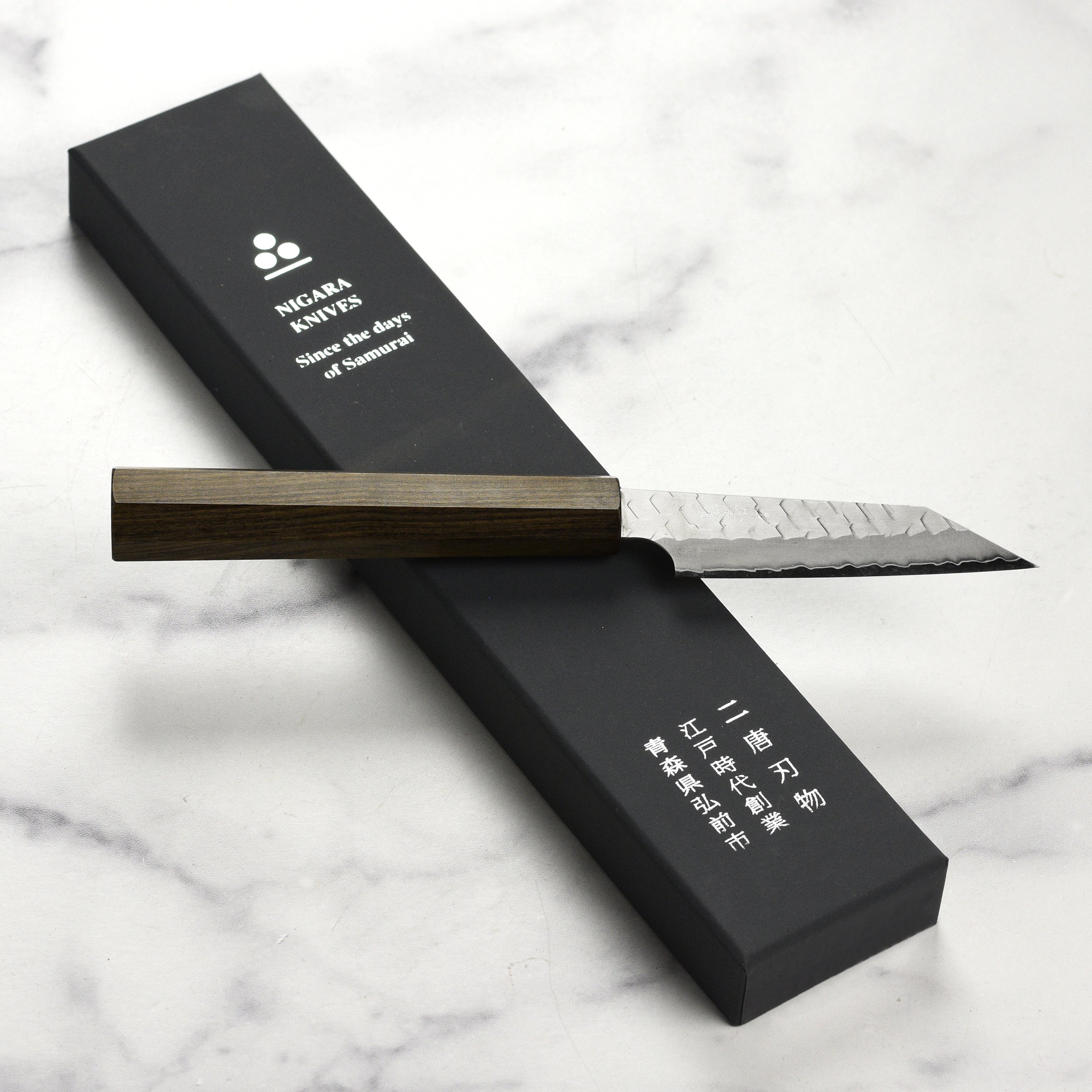 Complete view of the Nigara SG2 Migaki Tsuchime Kiritsuke Petty Knife on a wooden cutting board
