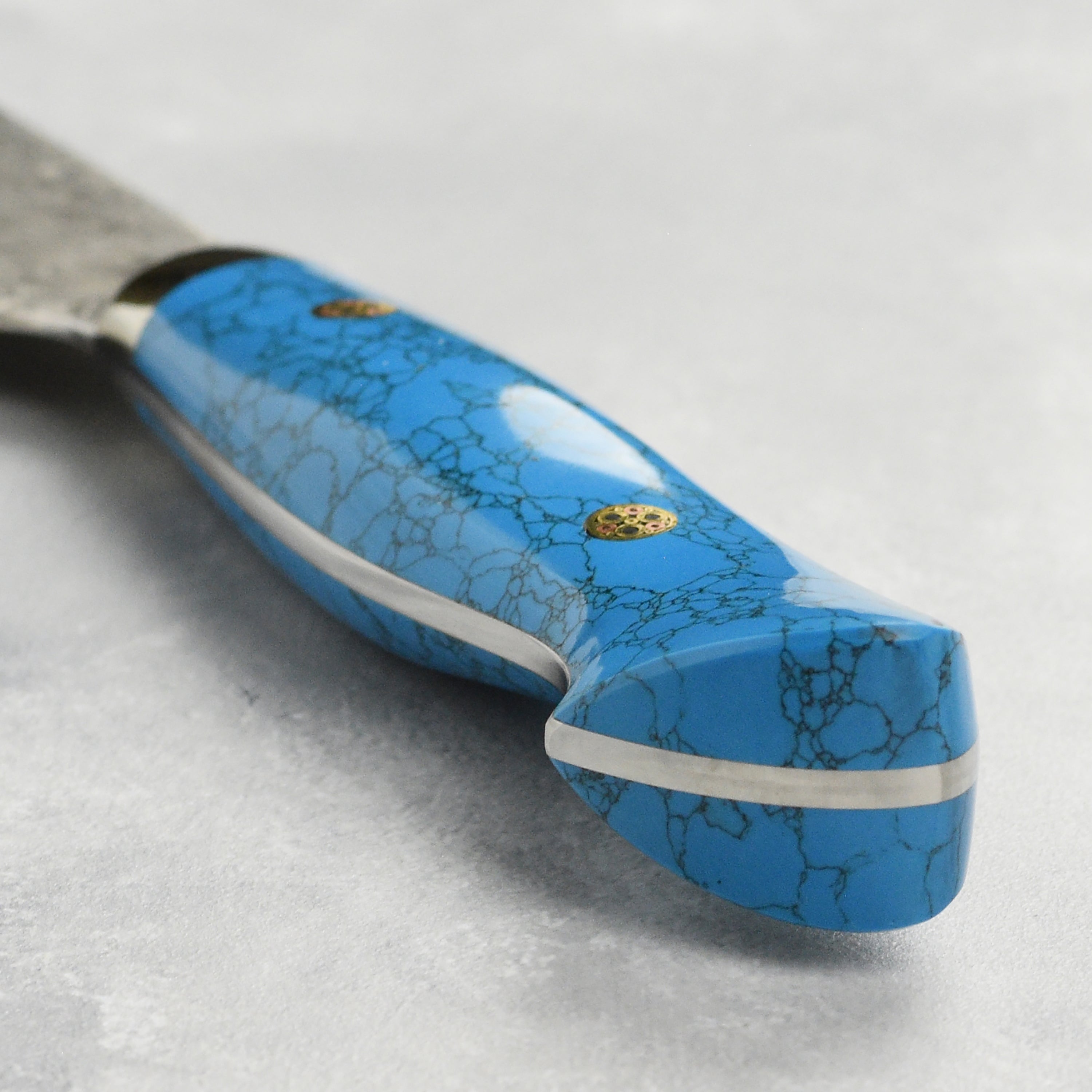 Side view of the gyuto knife with blue turquoise handle resting on a cutting board