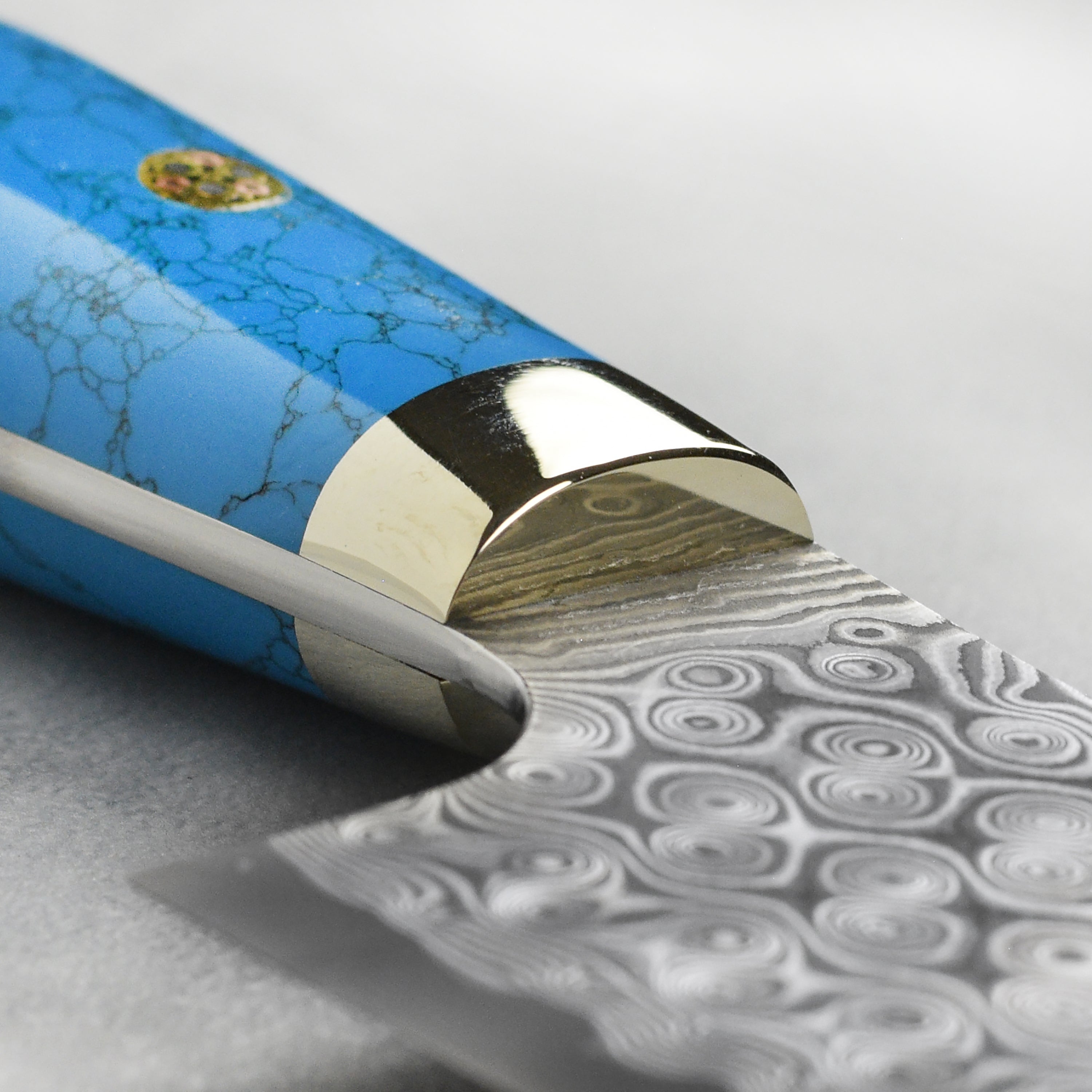 Side view of the gyuto knife with blue turquoise handle resting on a cutting board