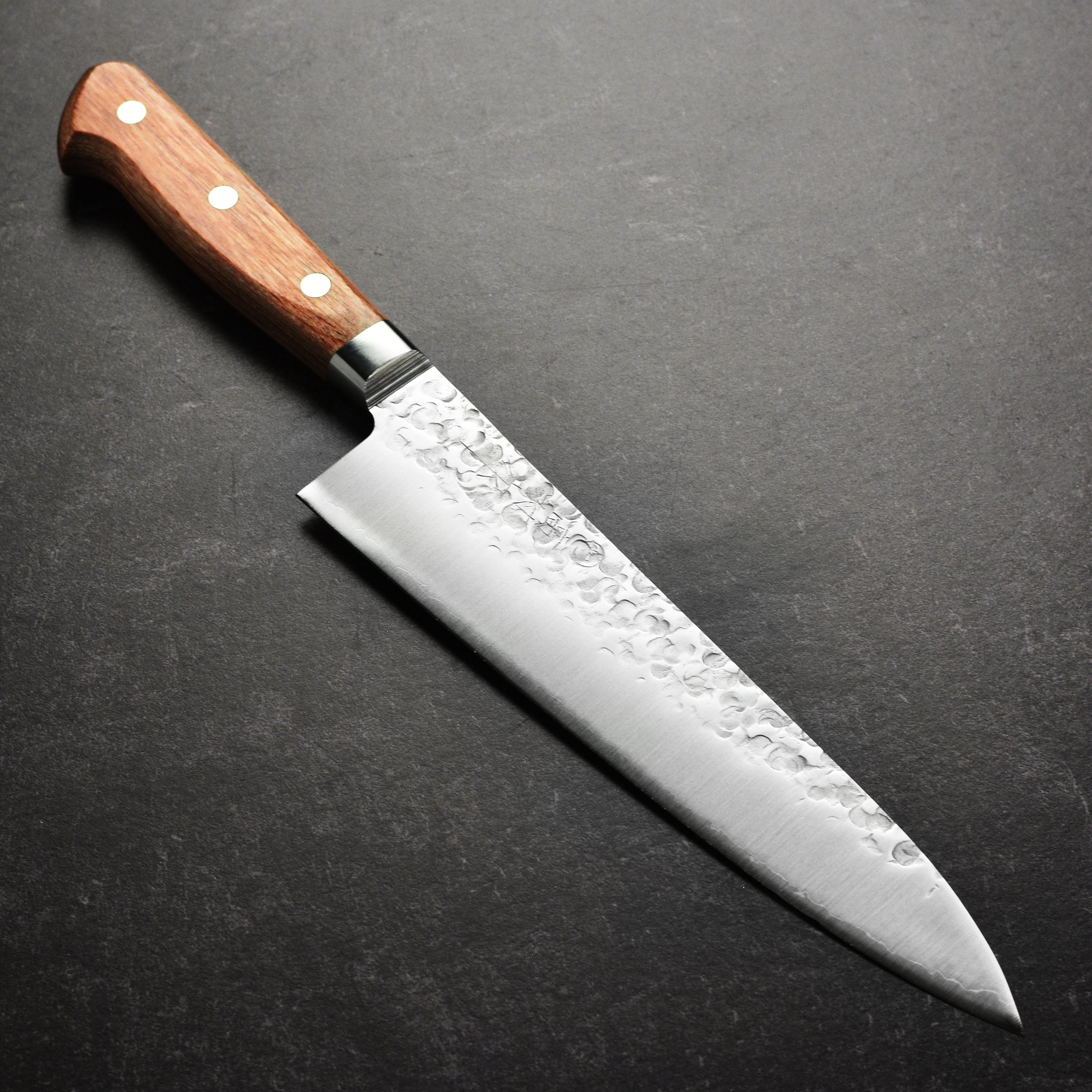 Takamura Chromax Tsuchime Gyuto Knife on a wooden cutting board, highlighting its sharp edge and unique finish.