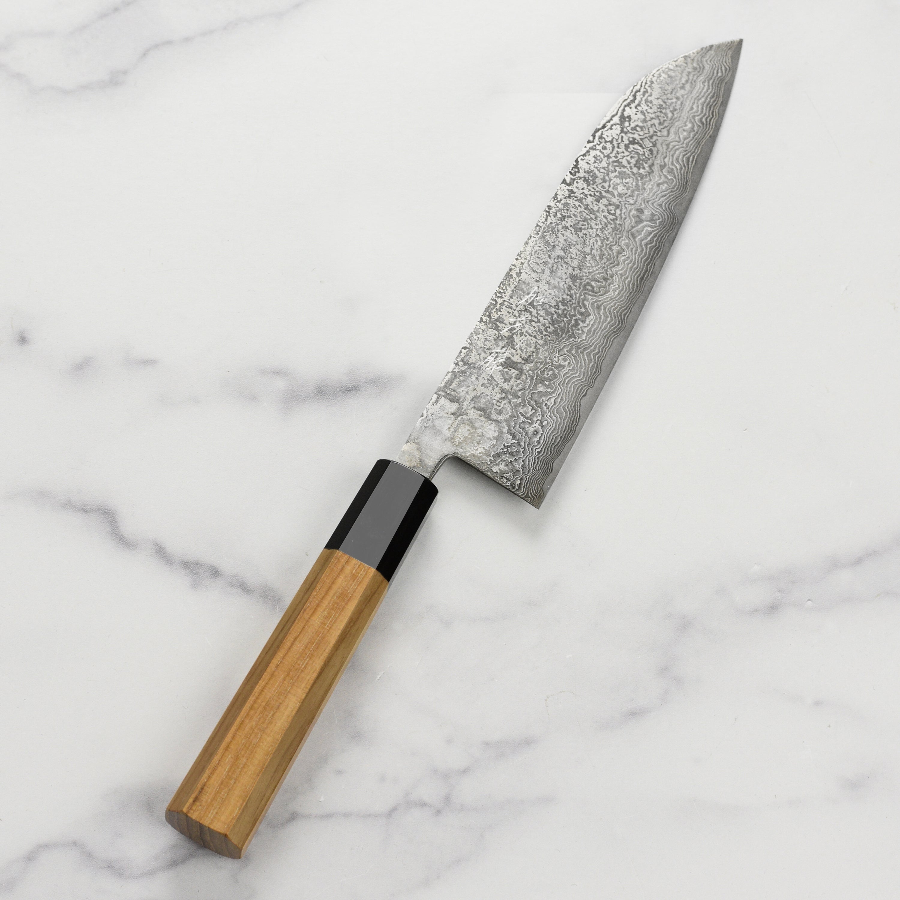Close-up view of the Shiro Kamo SG2 Santoku knife highlighting its Damascus steel pattern.