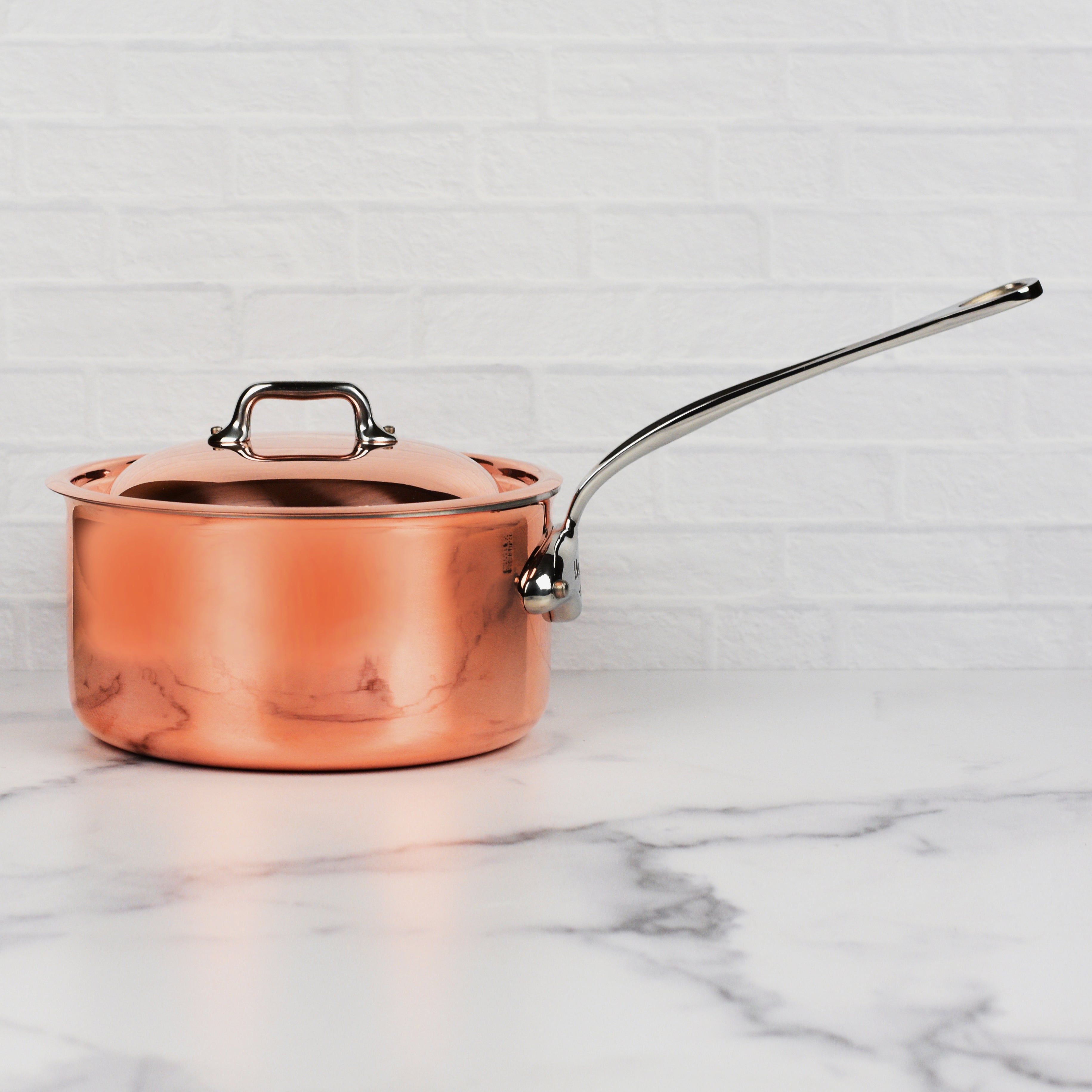 Close-up of stainless steel handles and flared rim of copper saucepan