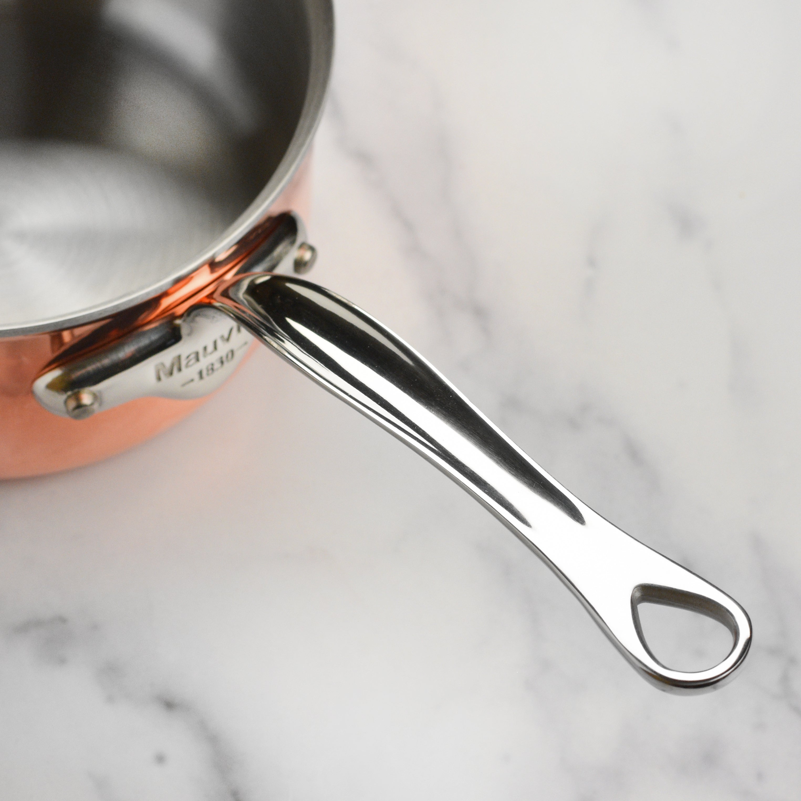 Close-up of Mauviel M6S copper saucepan on induction stovetop showing layered construction and sturdy handle