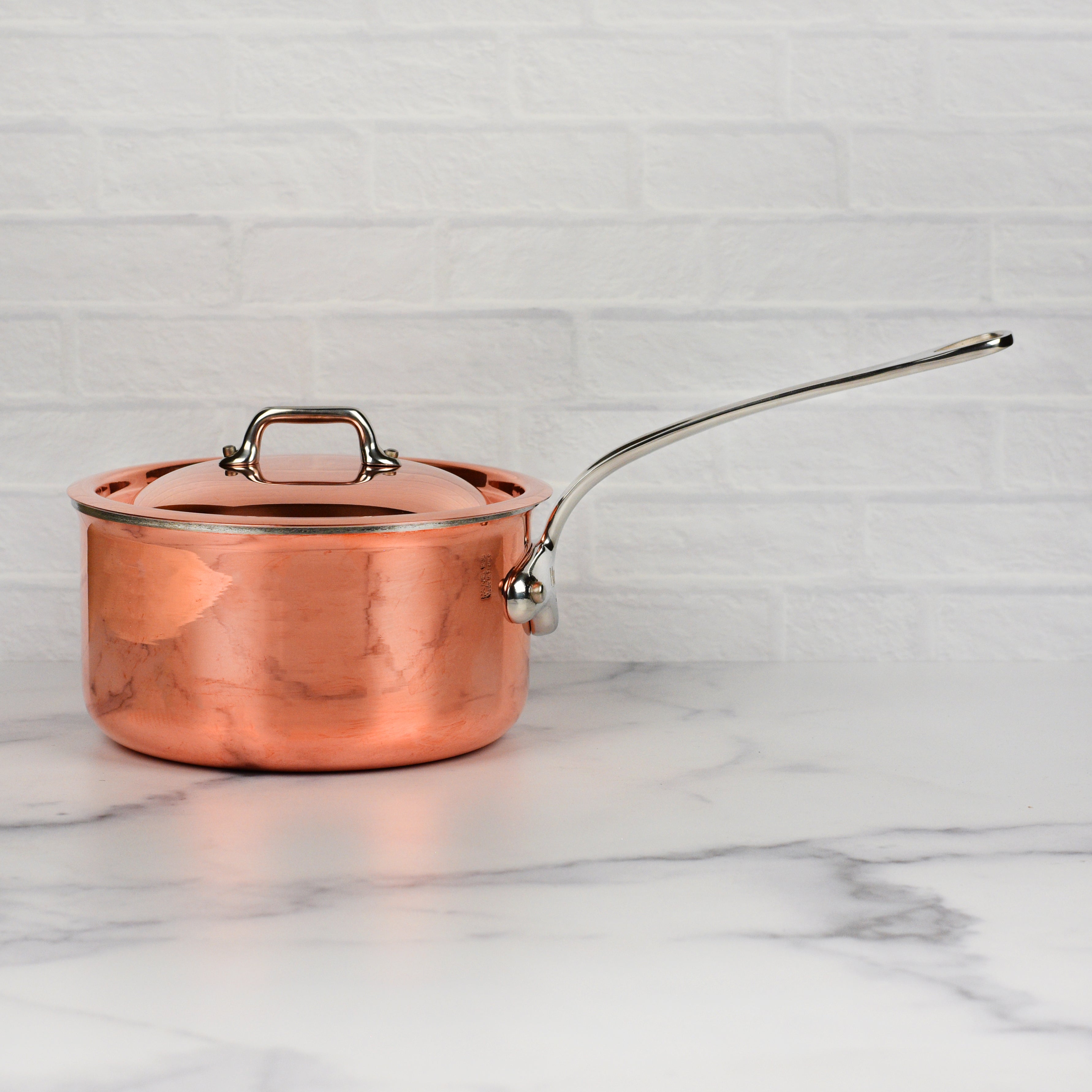 Overhead view of copper saucepan with lid beside fresh ingredients in a chef’s kitchen setting