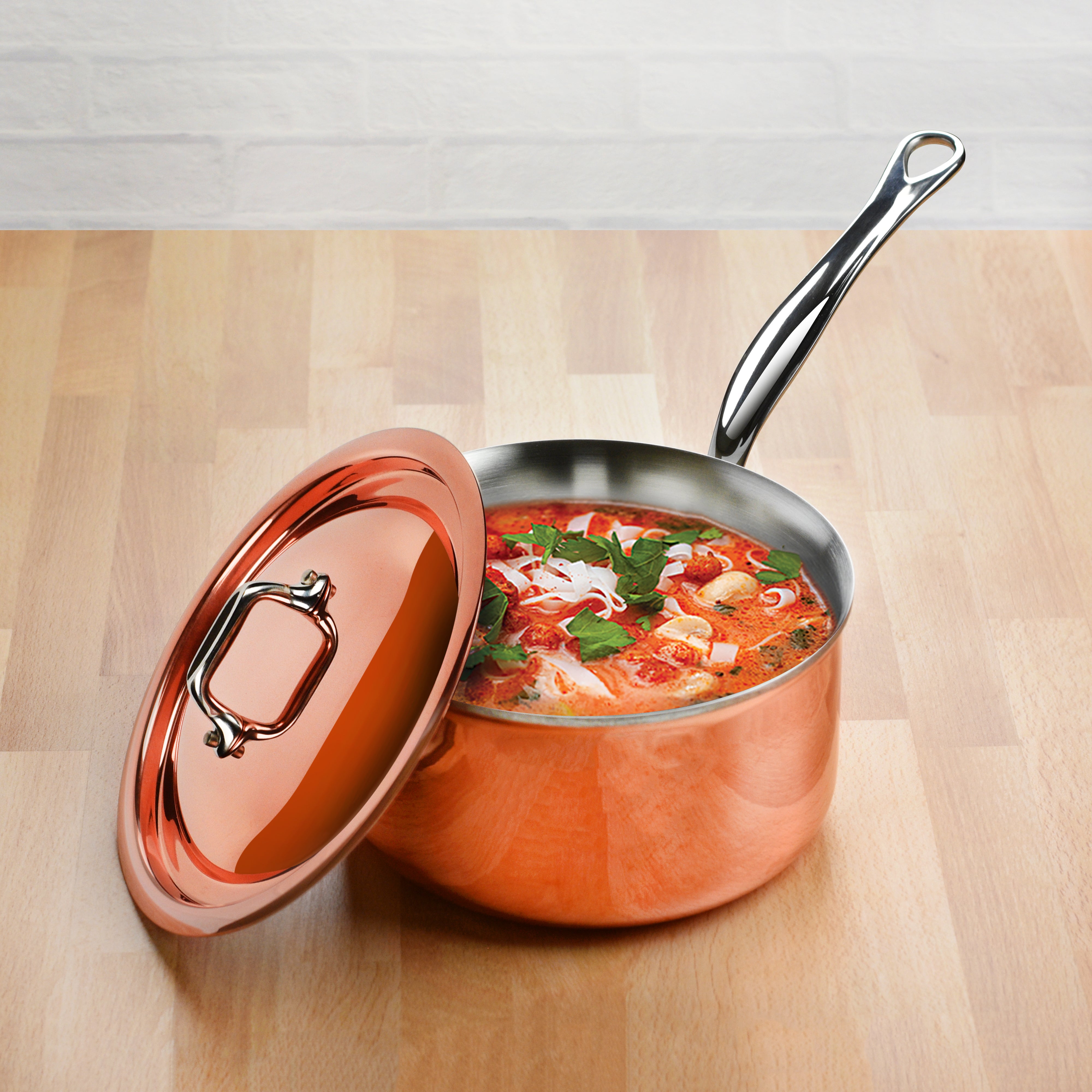 Overhead view of copper saucepan with lid beside fresh ingredients in a chef’s kitchen setting