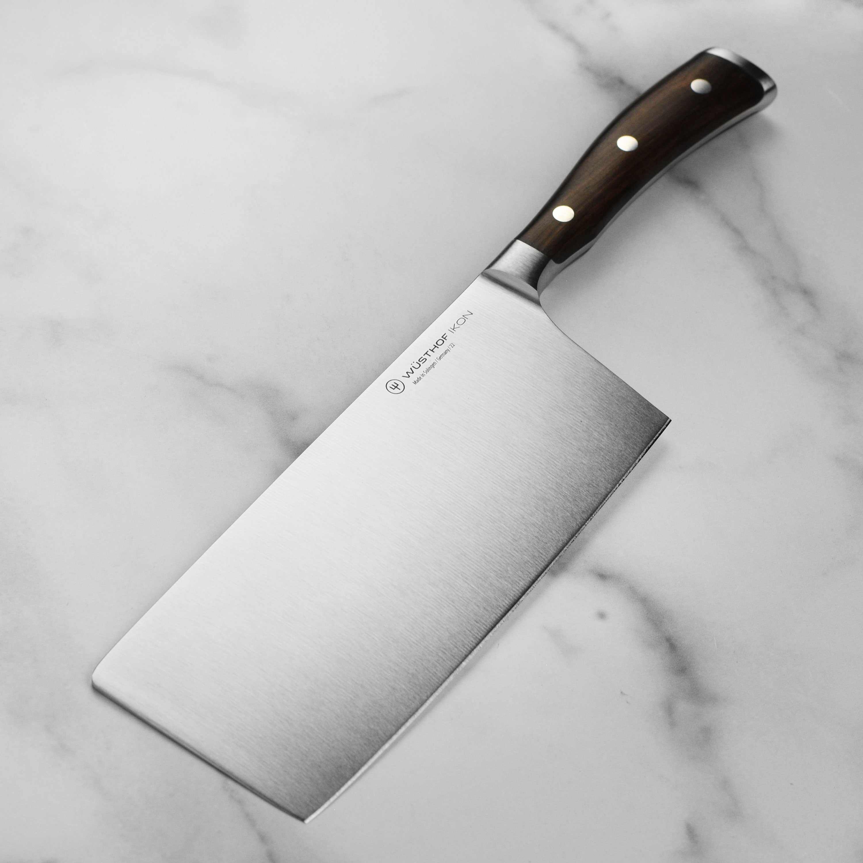 Wusthof Ikon Blackwood 7-Inch Chinese Chef Knife on a cutting board, displaying its sharp edge and ergonomic design.