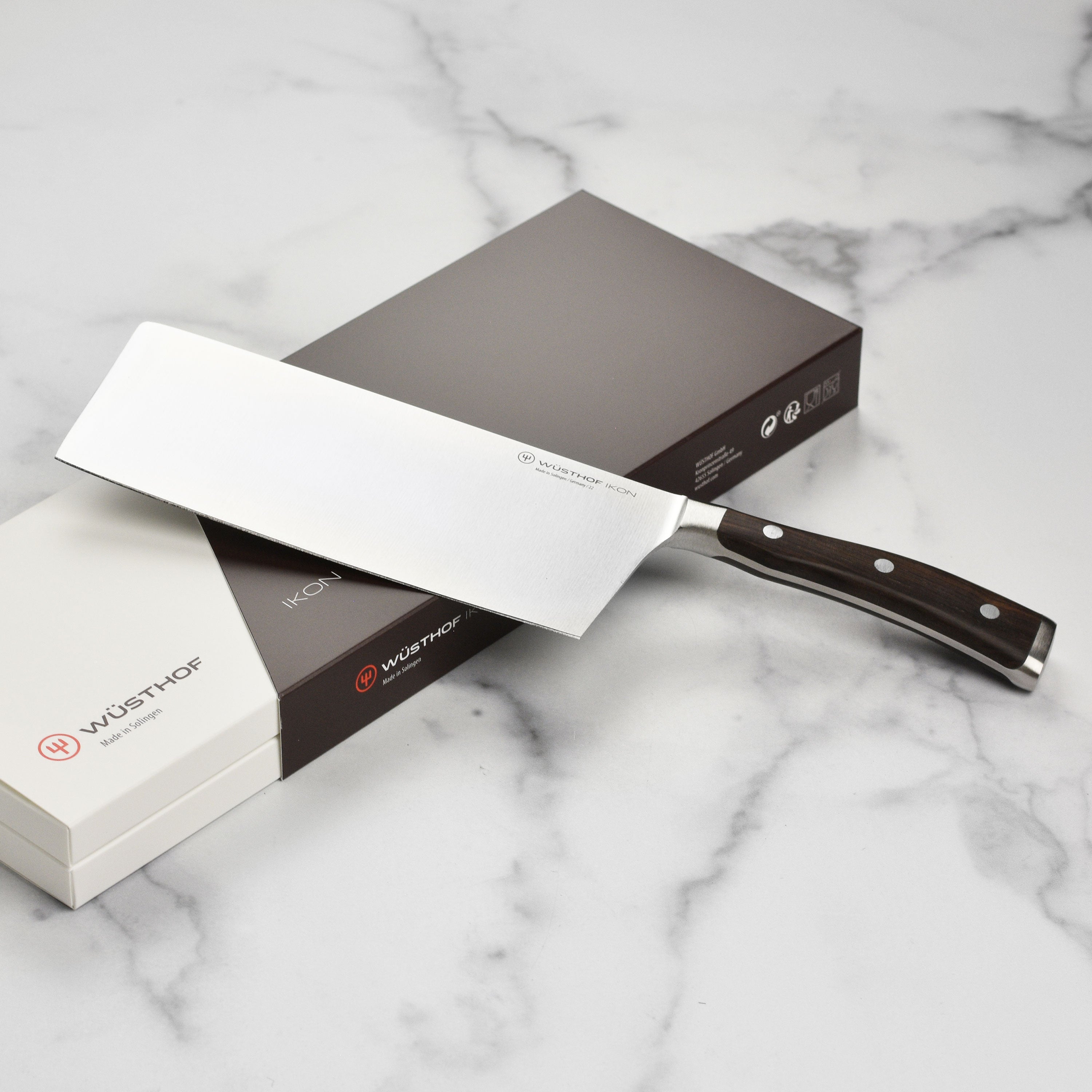 Wusthof Ikon Blackwood 7-Inch Chinese Chef Knife on a cutting board, displaying its sharp edge and ergonomic design.