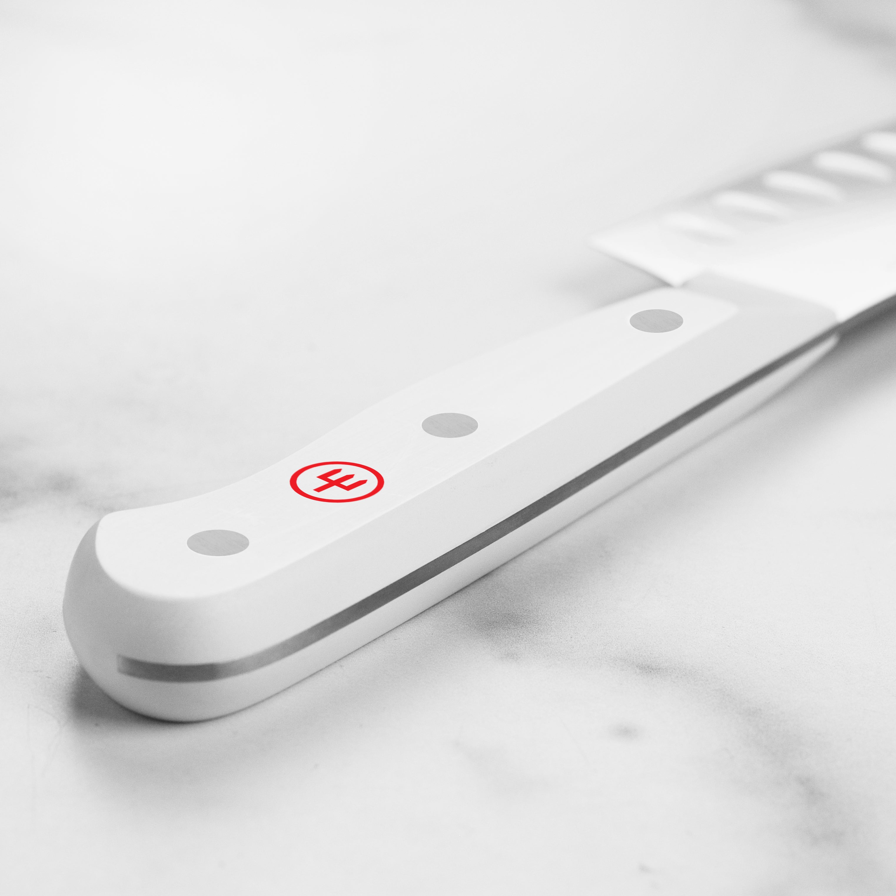 Wusthof 5 inch Santoku knife with white handle resting beside fresh herbs.