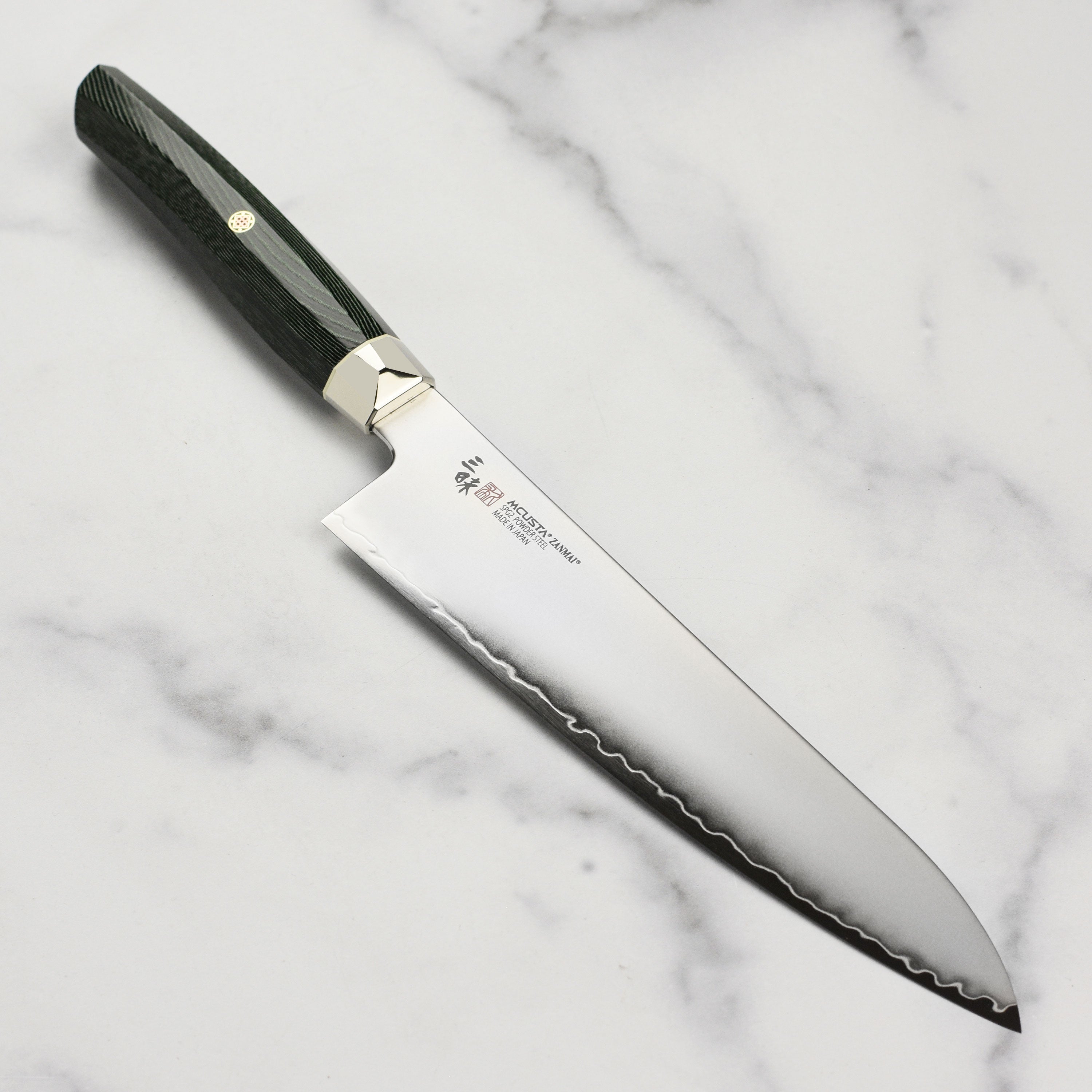 Zanmai Revolution SG2 kitchen knife displayed on a cutting board, showcasing its elegant green micarta handle.