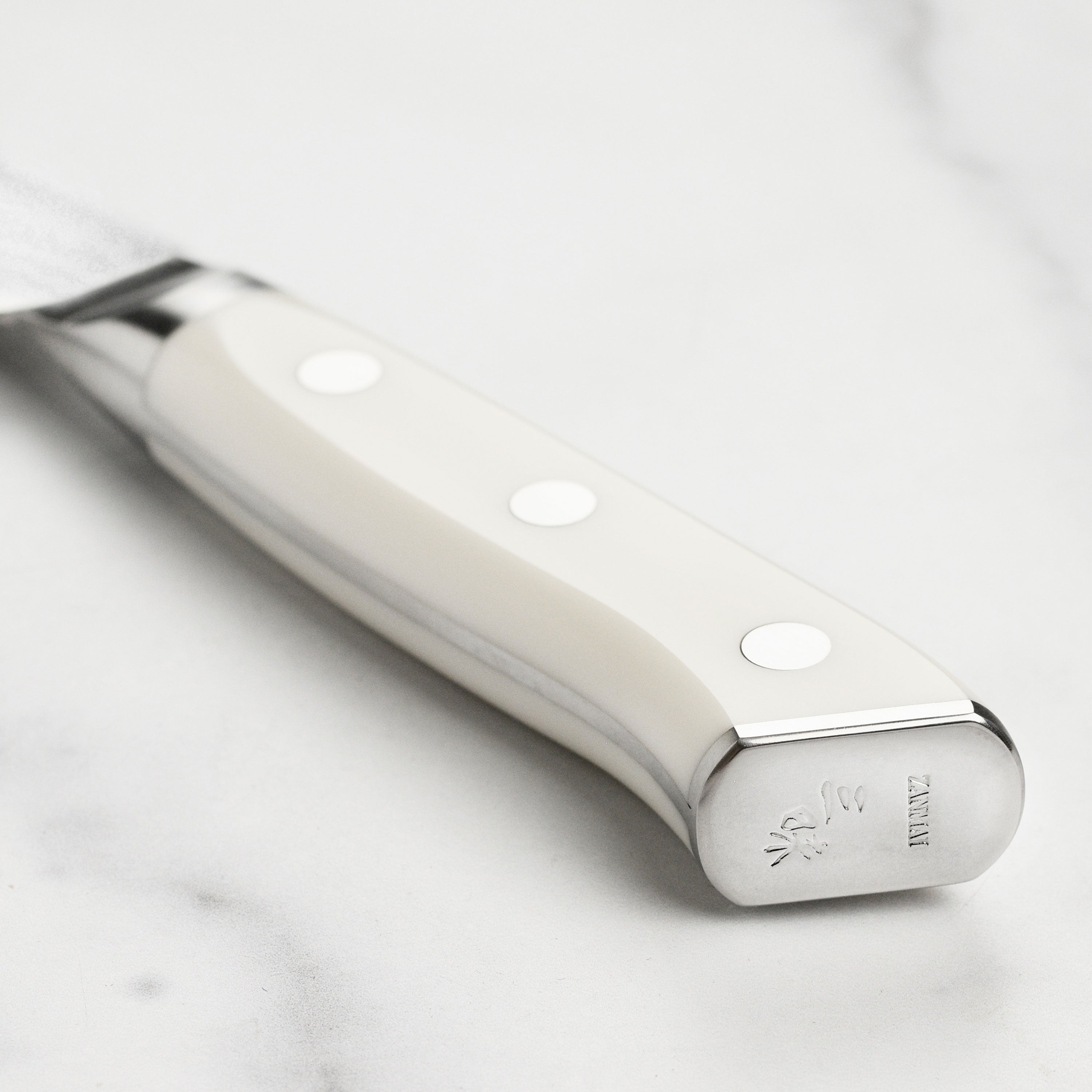 Ergonomic white Corian handle with engraved end cap on Zanmai Japanese damascus knife, perfect for detailed slicing.