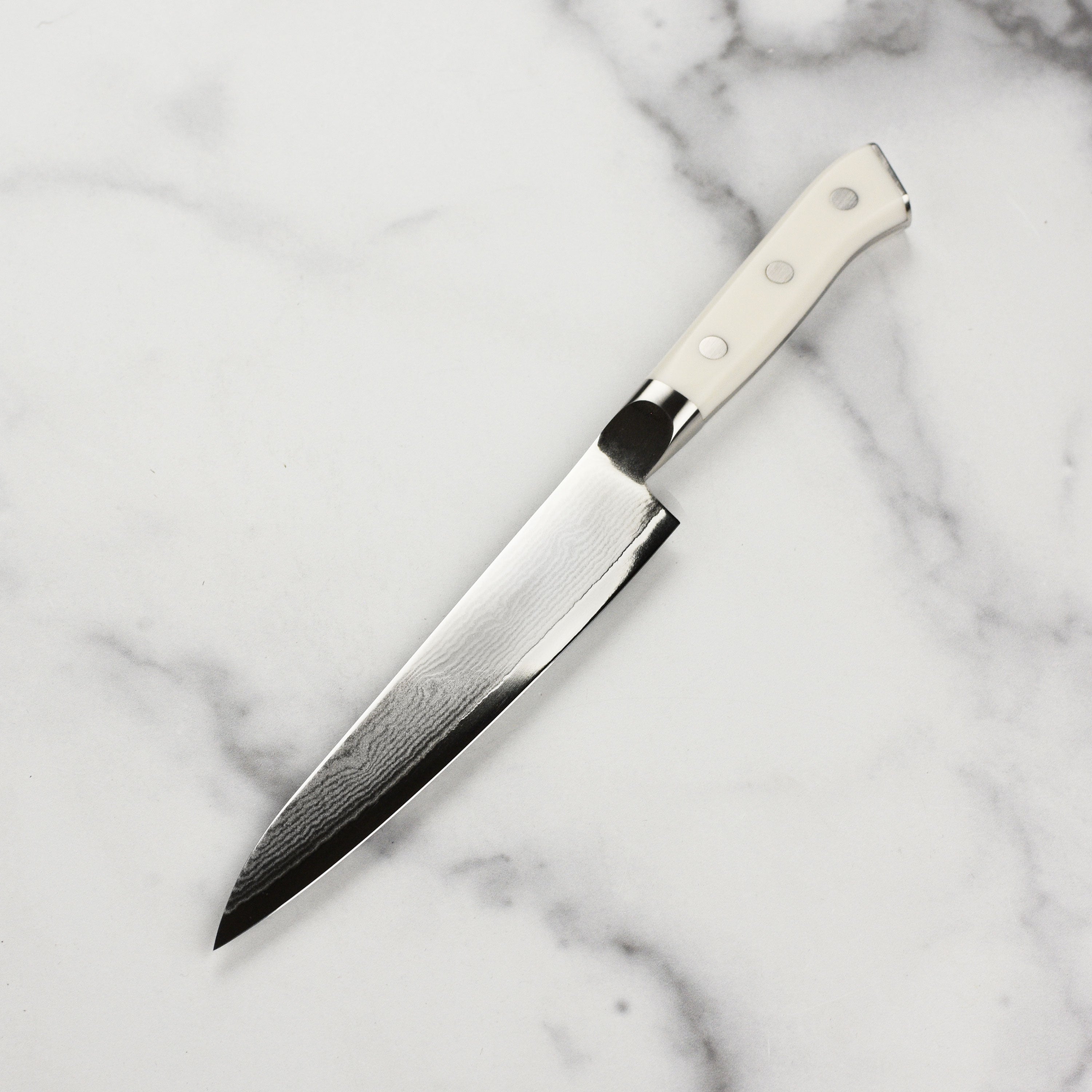 Ergonomic white Corian handle with engraved end cap on Zanmai Japanese damascus knife, perfect for detailed slicing.
