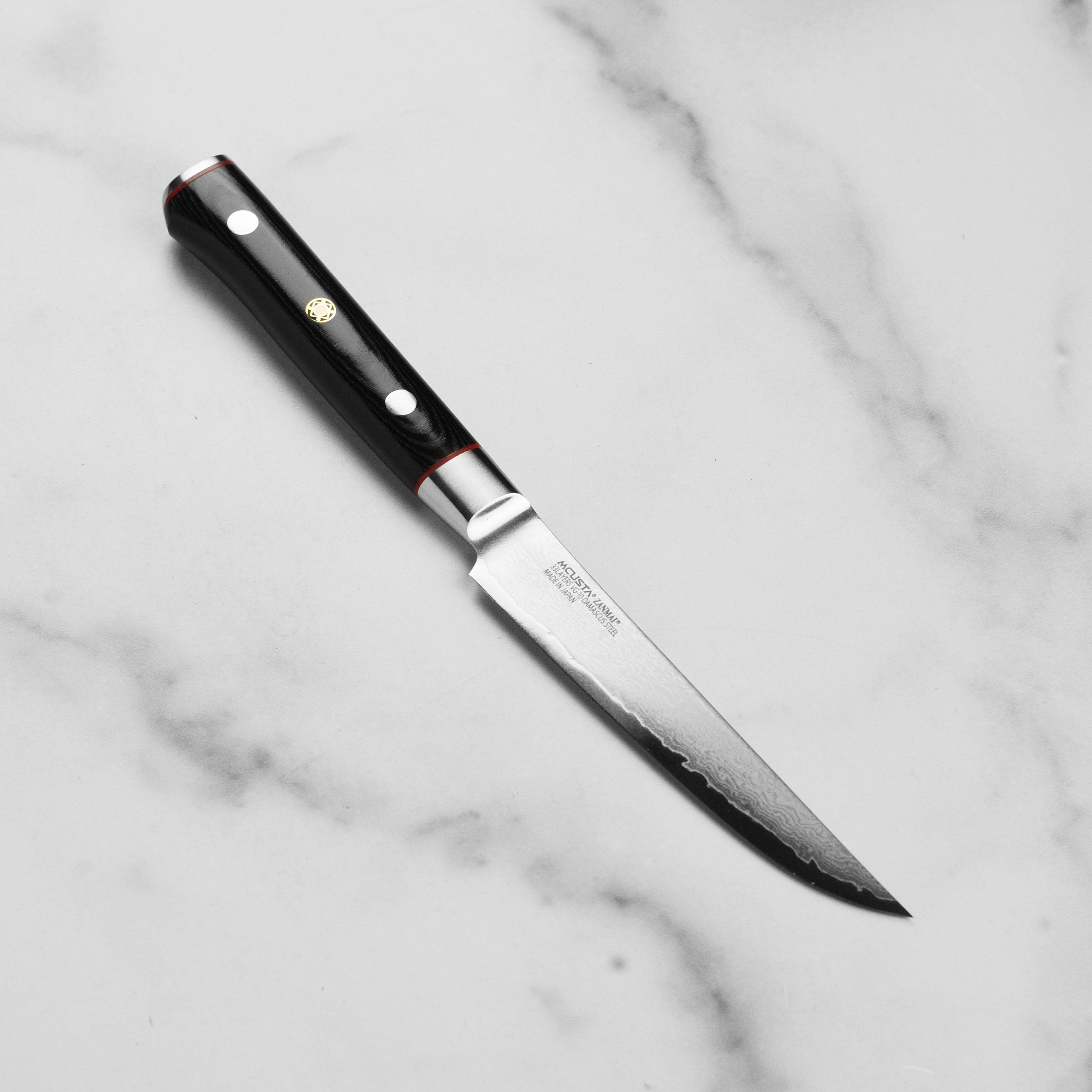 Zanmai Classic Pro Zebra Damascus Steak Knife on a wooden cutting board, highlighting the intricate blade pattern.