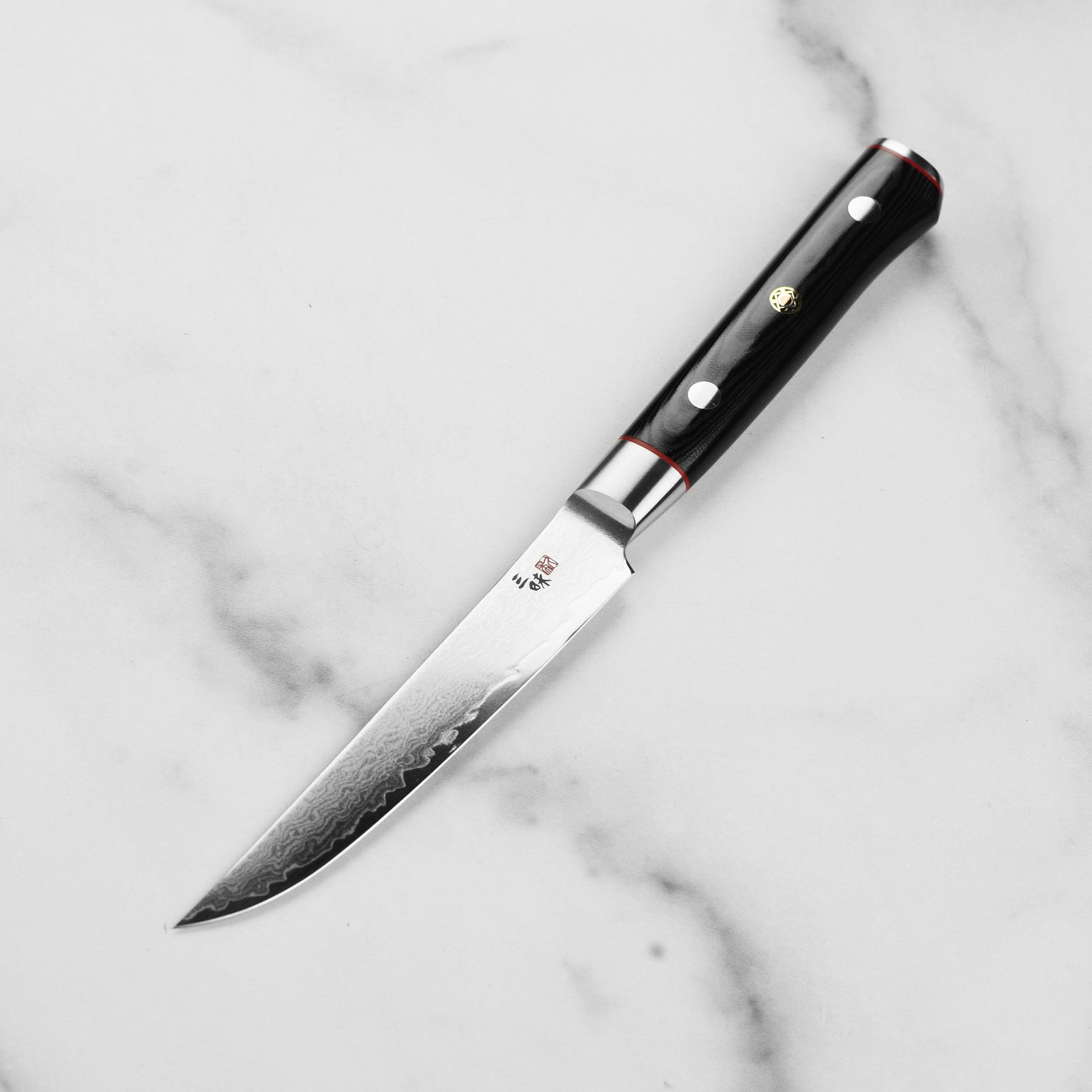 Close-up of the black Micarta handle of the Zanmai Damascus knife, showing the red spacers and Japanese mosaic accent pin.