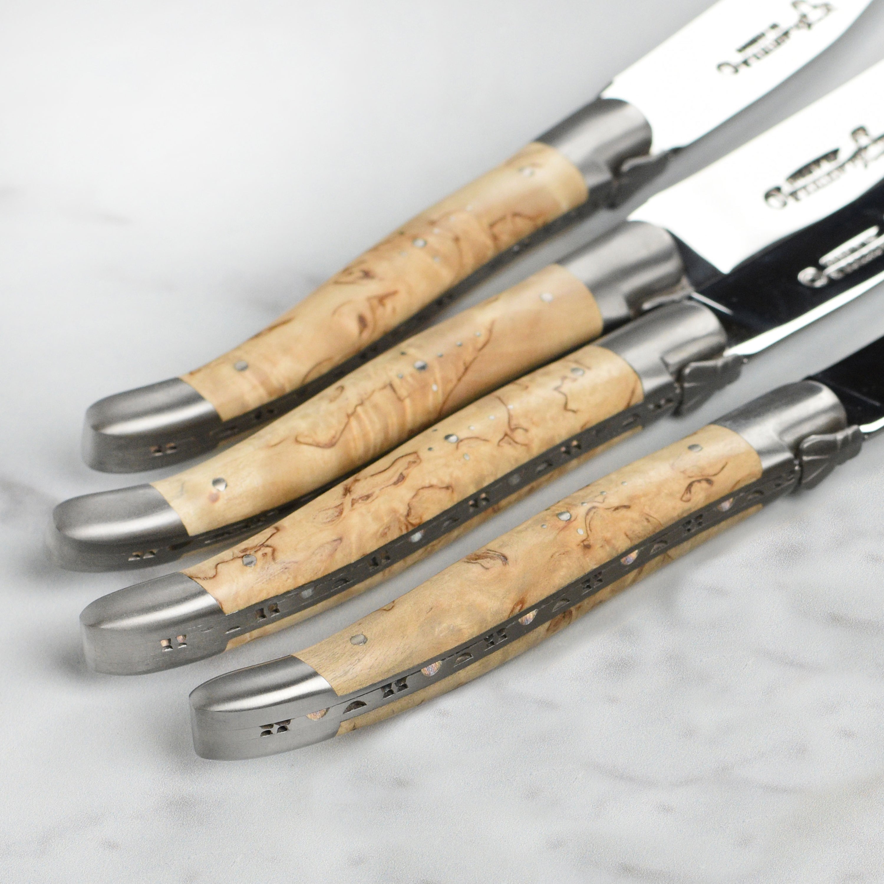 Close-up of the sharp stainless steel blade and birchwood handle of a Laguiole knife.