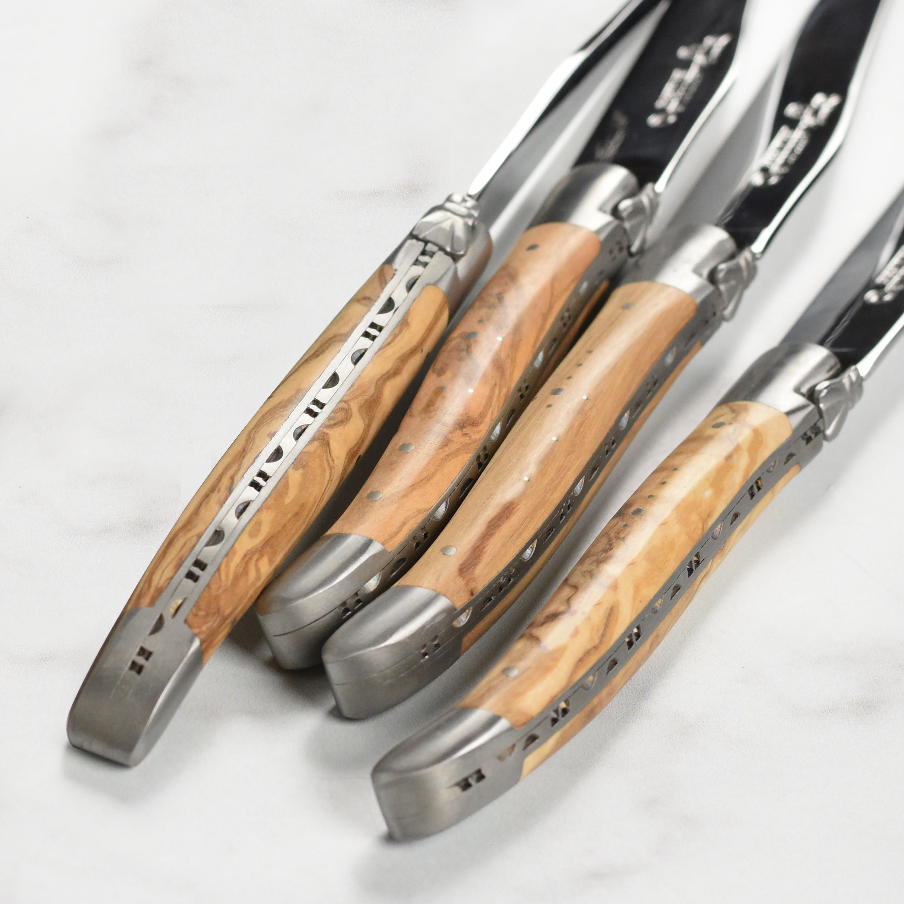 Set of four stainless steel steak knives with olive wood handles on a dining table