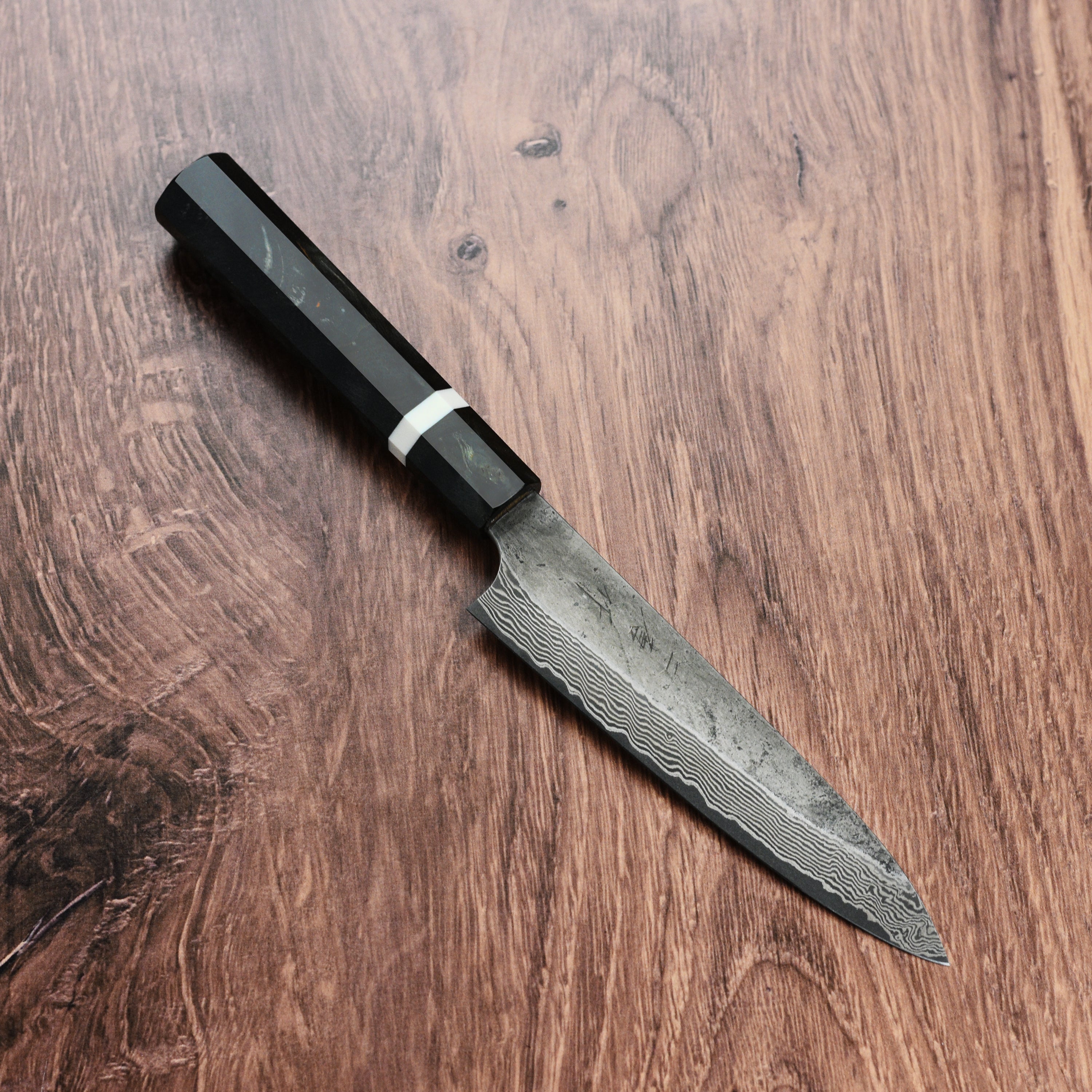 The Premium Nigara Ginsan Damascus Petty Knife in action, slicing fresh vegetables on a wooden cutting board.