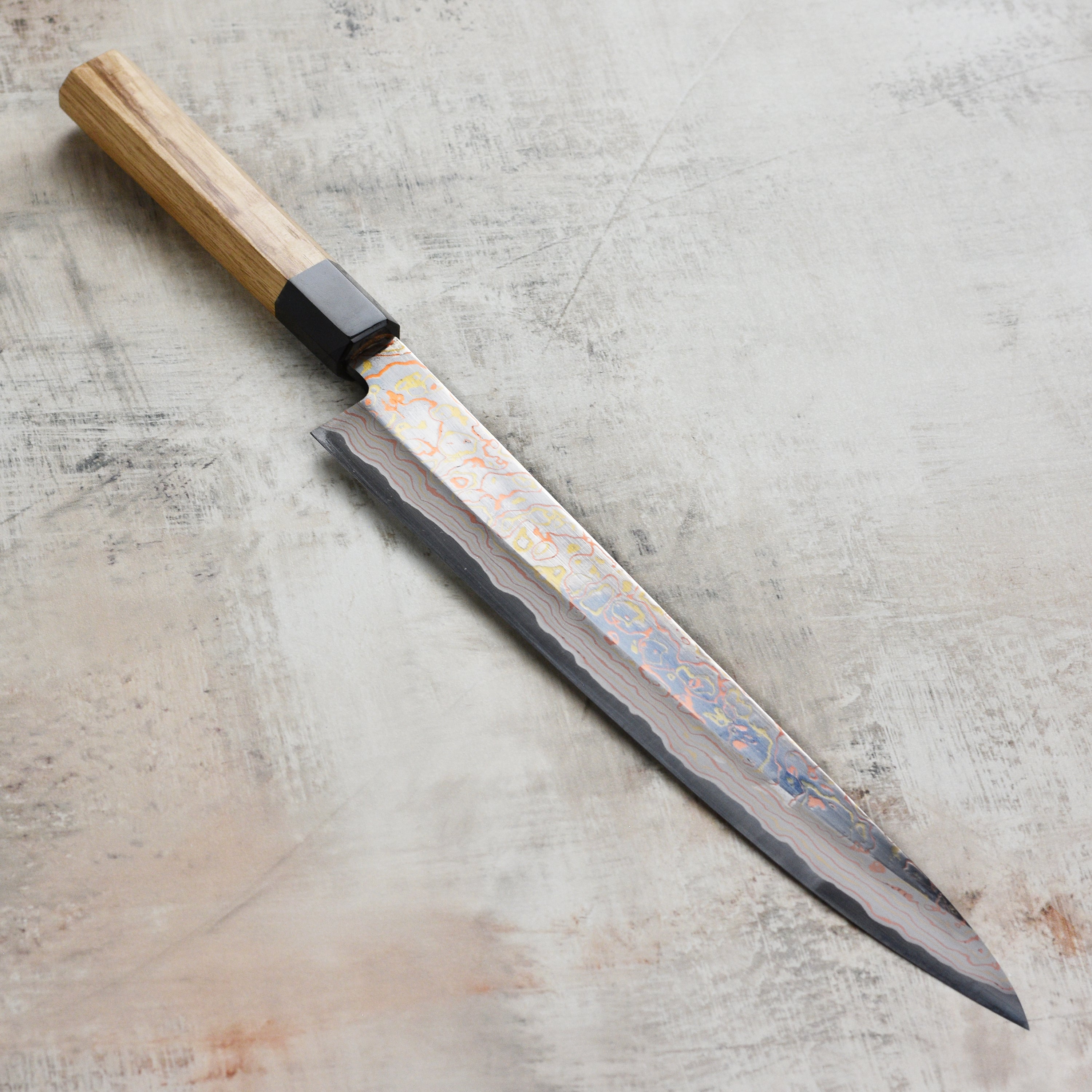 Elegant Hinoura Damascus sujihiki resting on a wooden cutting board