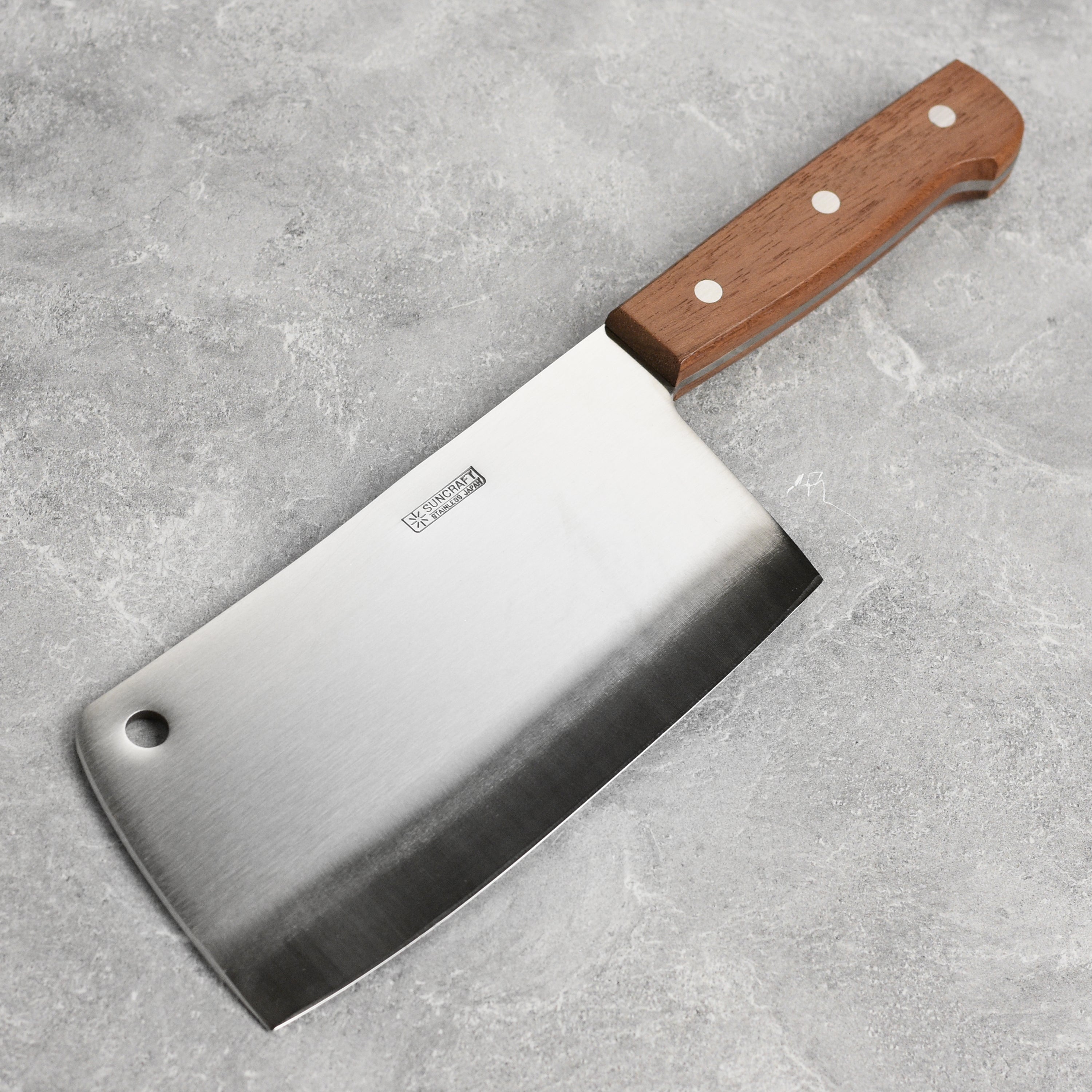 Suncraft meat cleaver in action, chopping vegetables on a wooden cutting board.