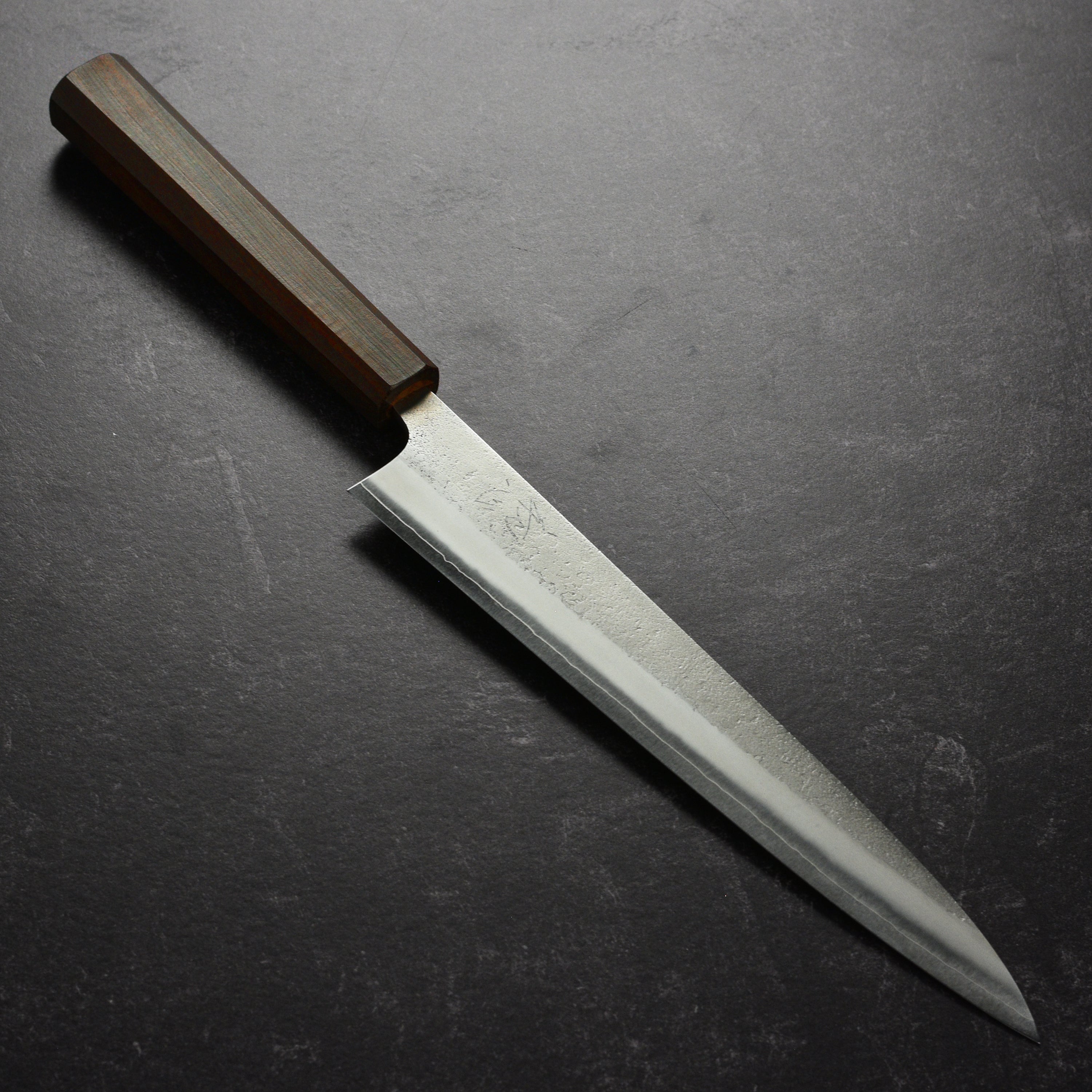 Yoshikane SKD Nashiji stainless clad sujihiki knife slicing fish on a cutting board