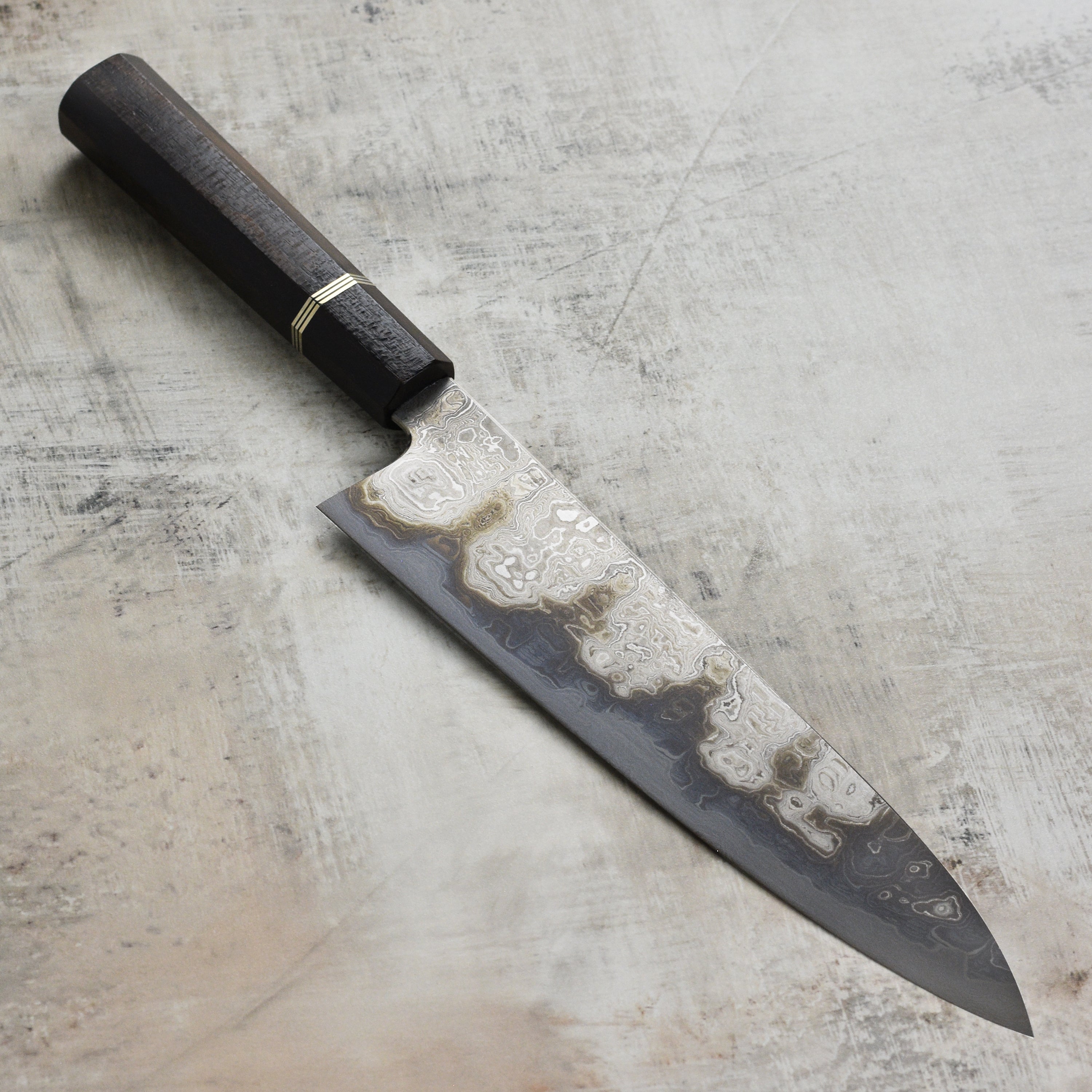 Shiomachi Aogami Gyuto knife showcasing its Damascus blade and ergonomic handle from a side angle.
