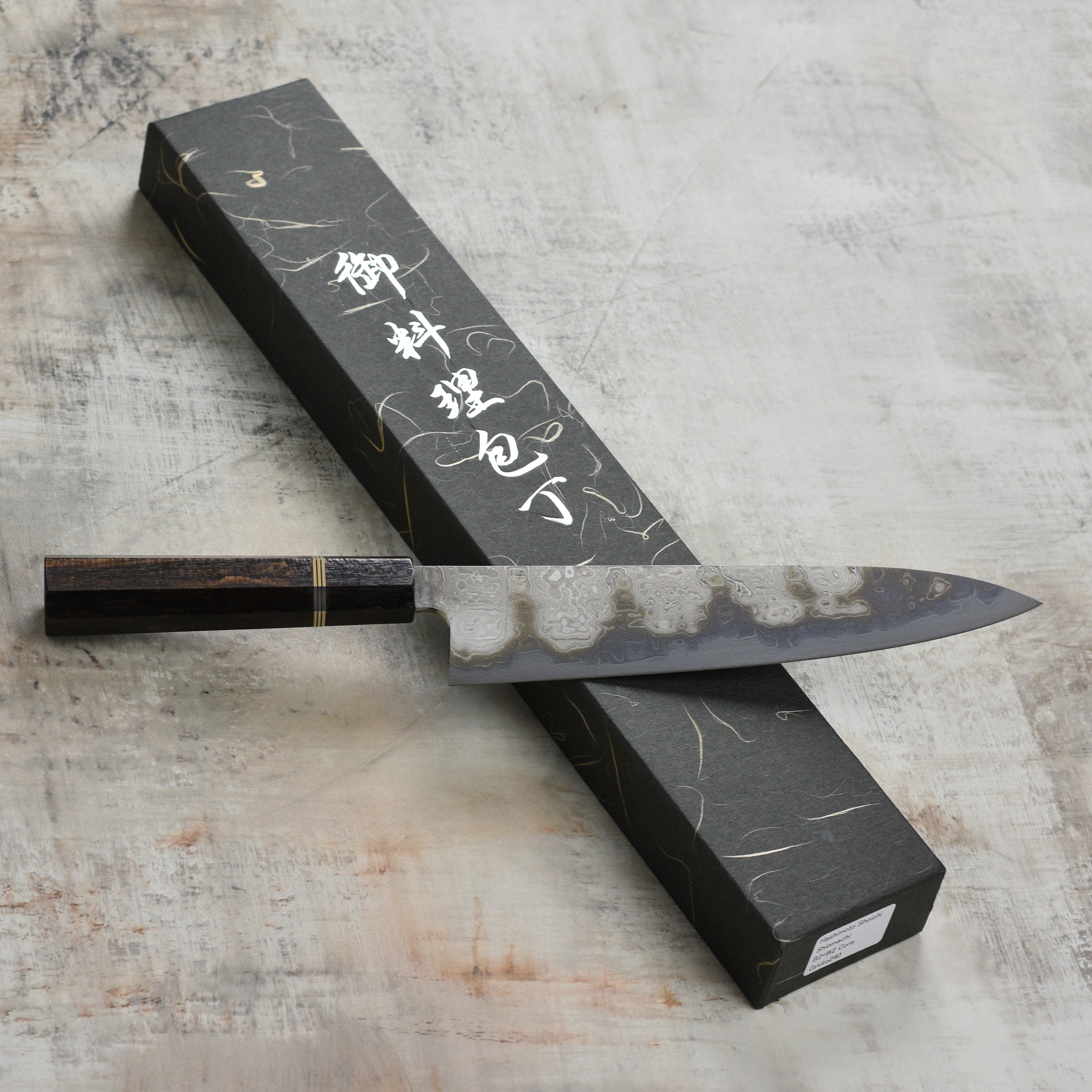 Shiomachi Aogami Gyuto knife showcasing its Damascus blade and ergonomic handle from a side angle.