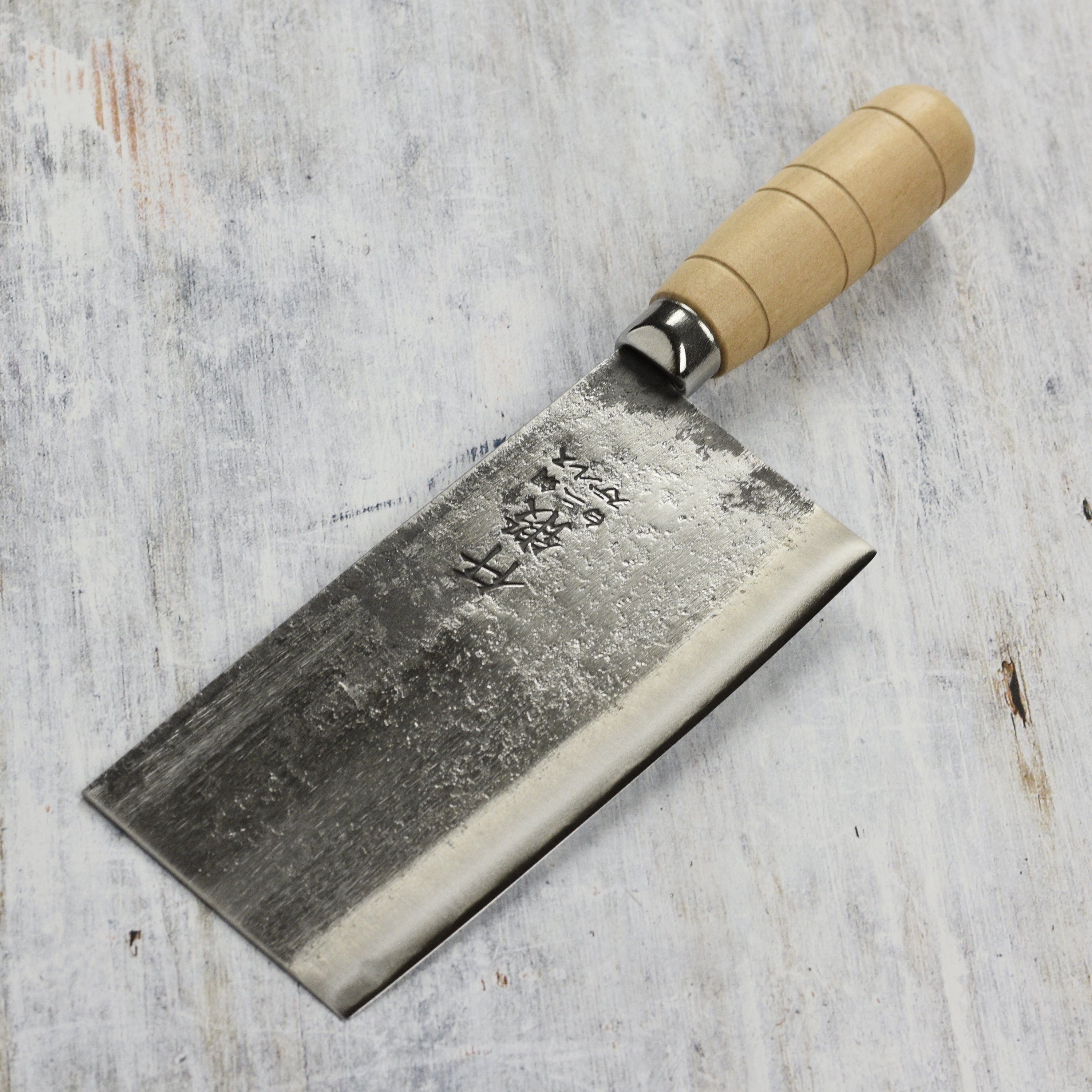 Rustic hand-forged carbon steel Chinese cleaver showcasing its migaki finish and traditional barrel handle.