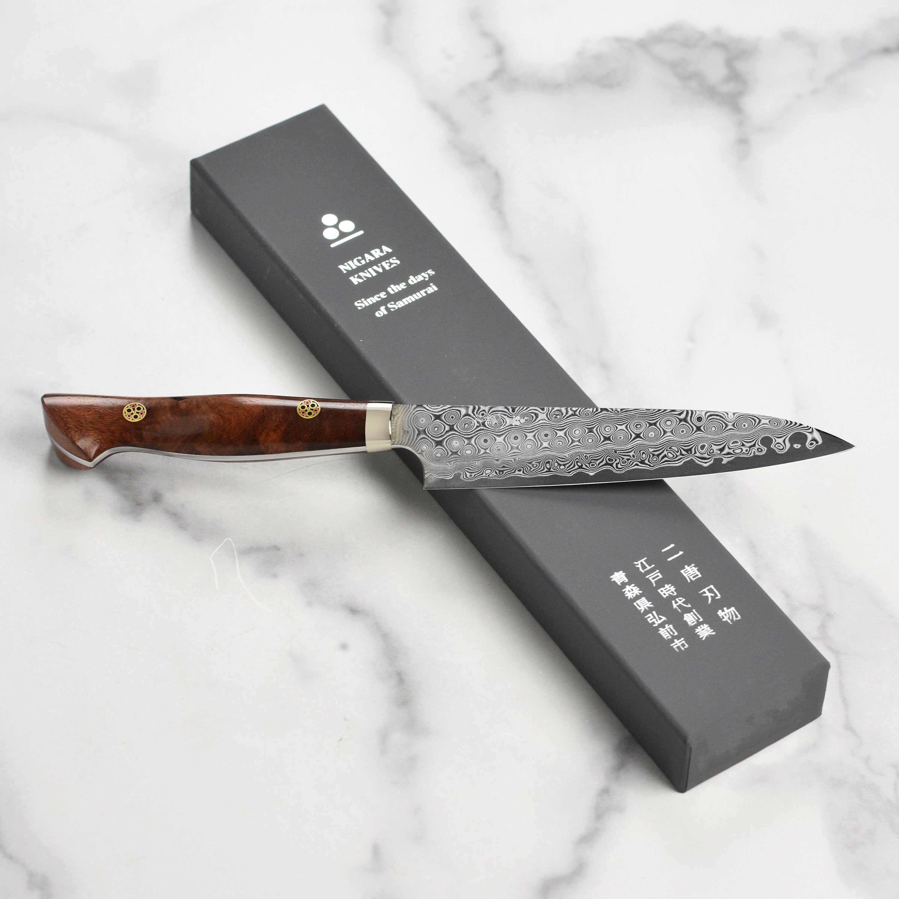 Nigara Anmon SG2 Damascus petty knife with quince wood handle on a wooden cutting board
