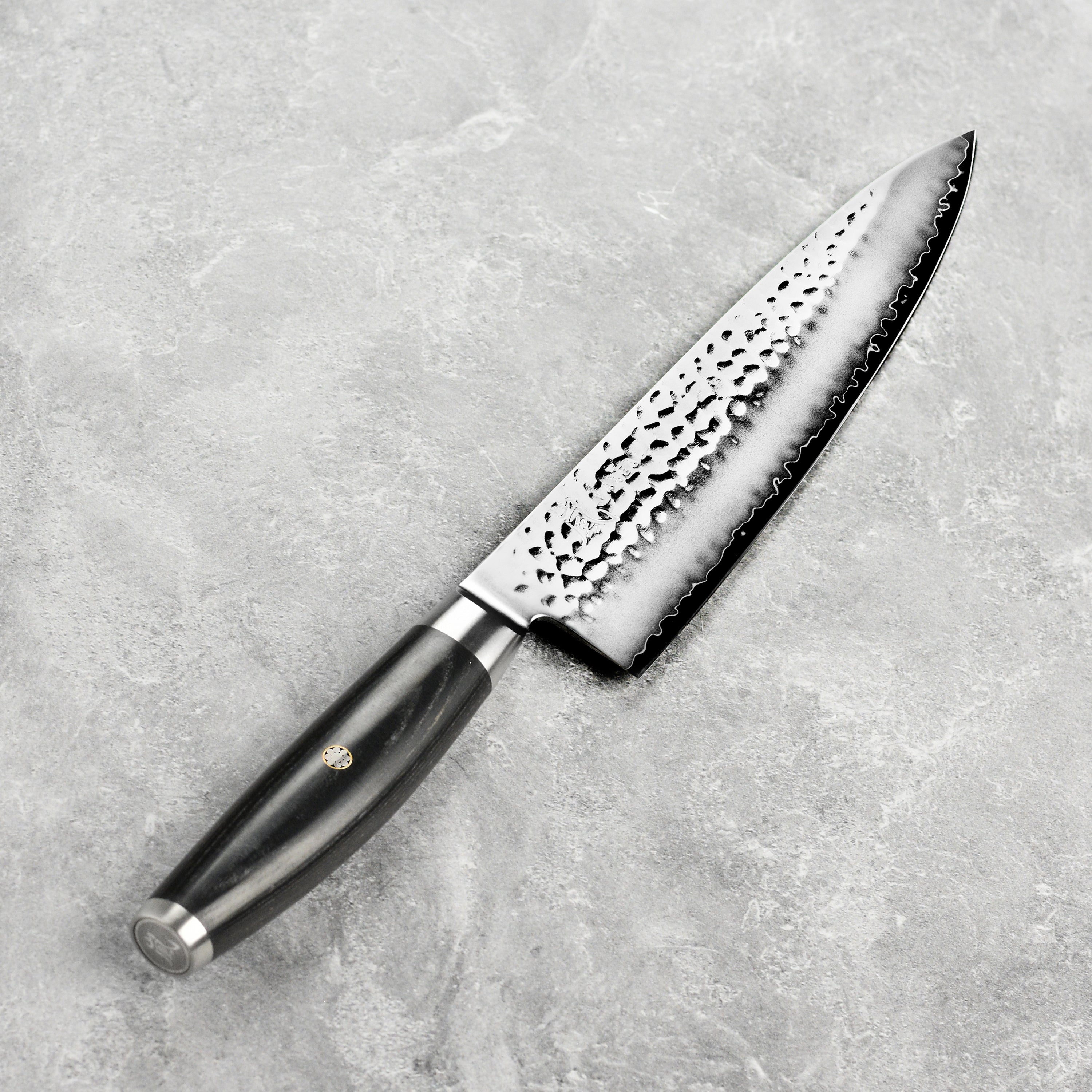 Chef using Yaxell Ketu Chefs Knife to chop vegetables in a bright kitchen.