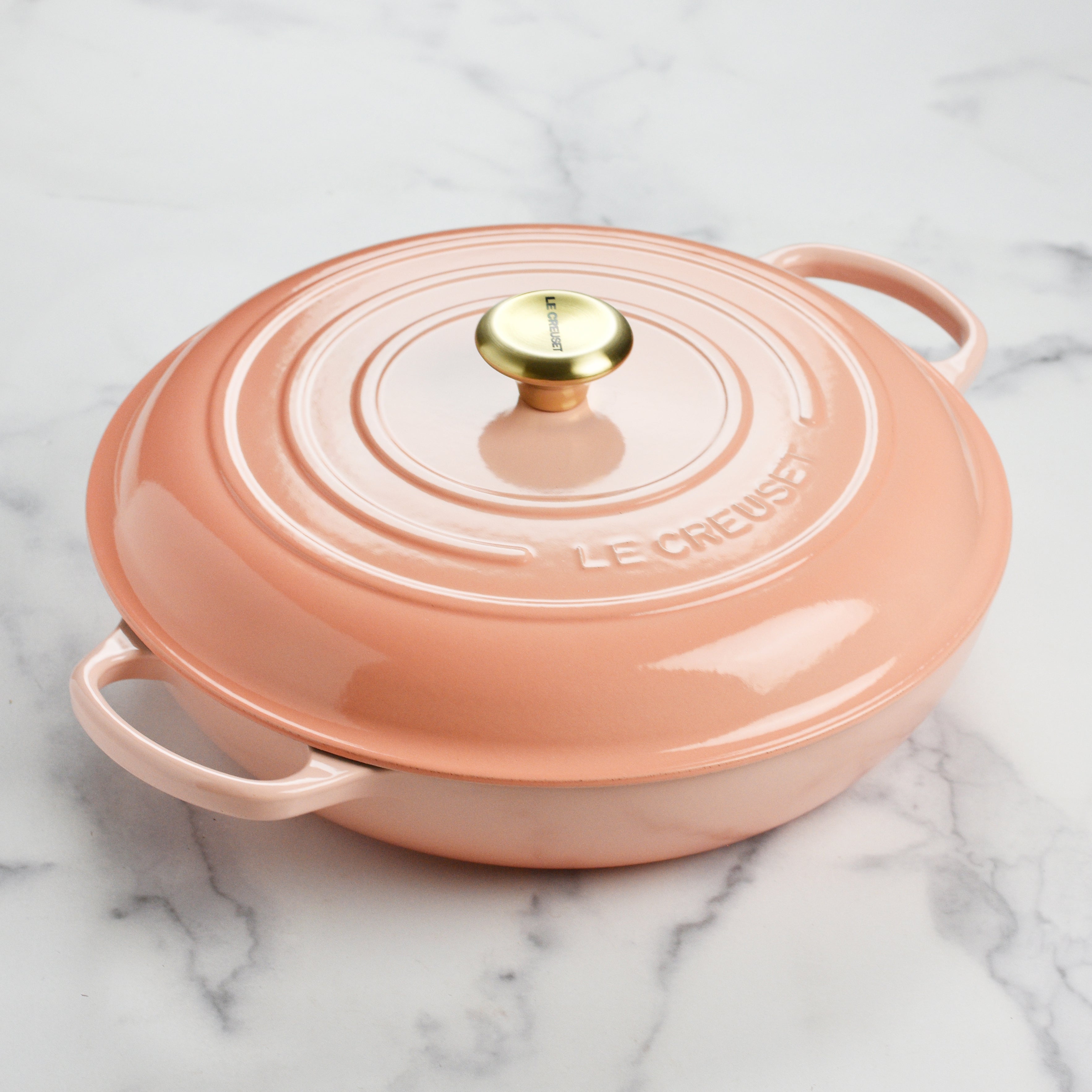 A close-up of the light gold stainless steel knob on the Le Creuset braiser, emphasizing its functional design.
