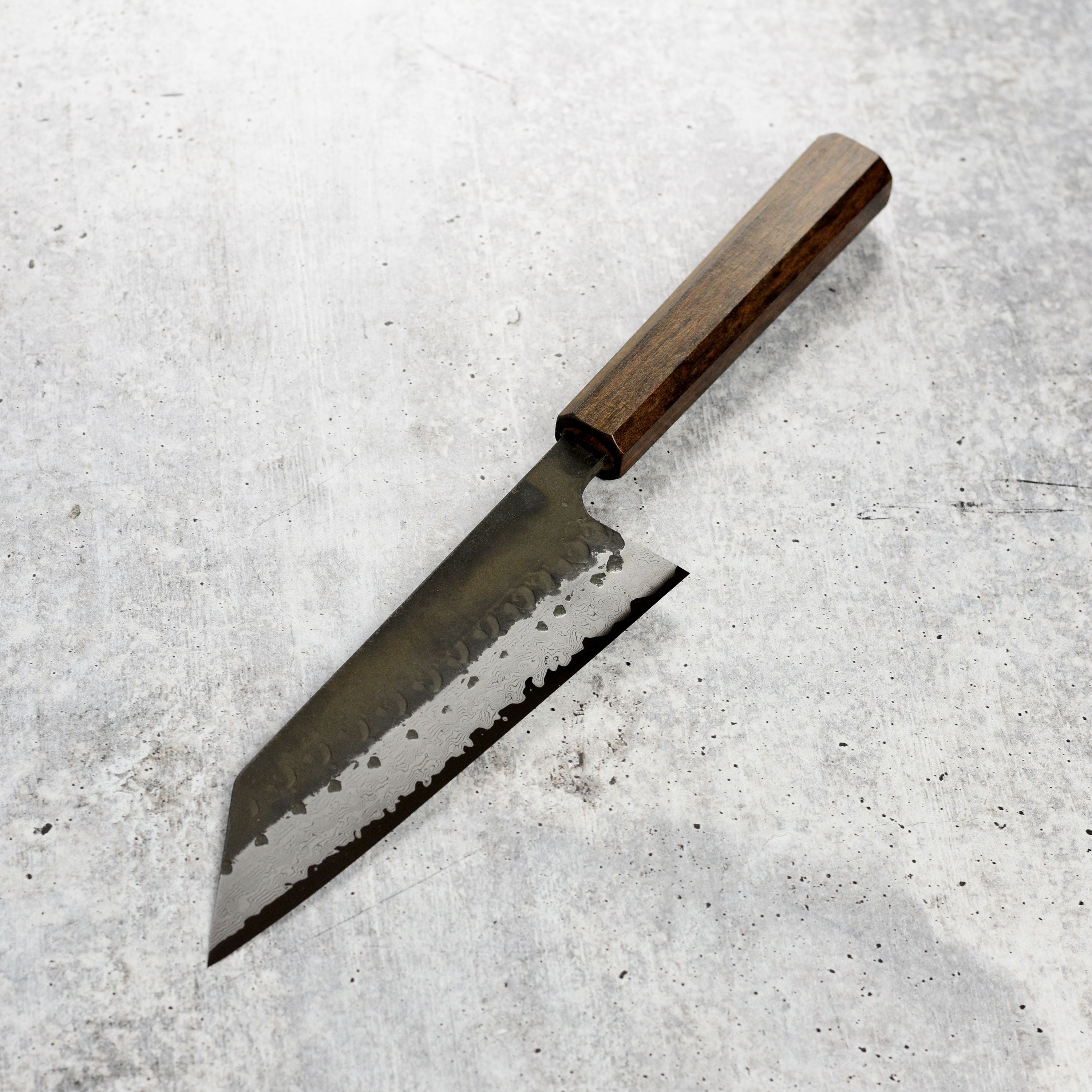 Hatsukokoro Shinkiro Aogami Super Damascus bunka knife with kurouchi finish displayed on a cutting board