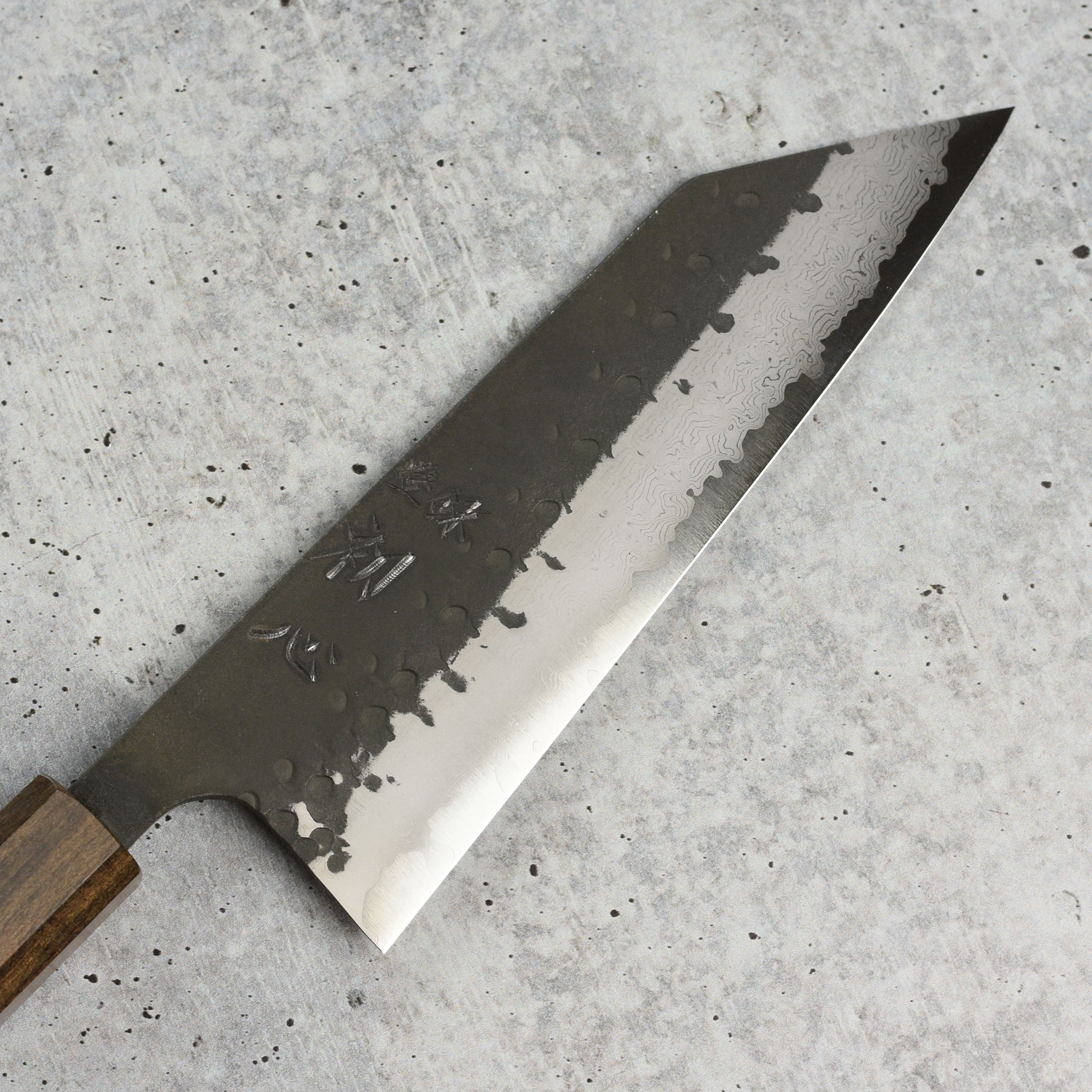 Hatsukokoro Shinkiro Aogami Super Damascus bunka knife with kurouchi finish displayed on a cutting board